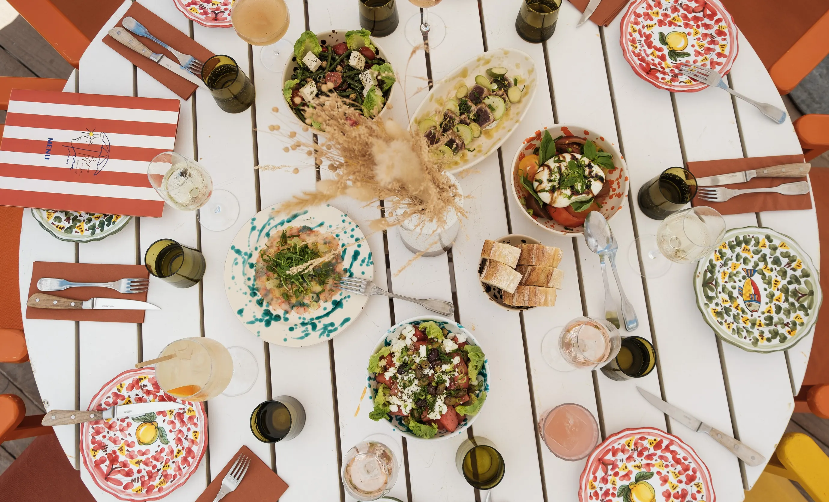Aerial view of a communal outdoor table featuring various Mediterranean dishes and cocktails at an Experimental Group restaurant.
