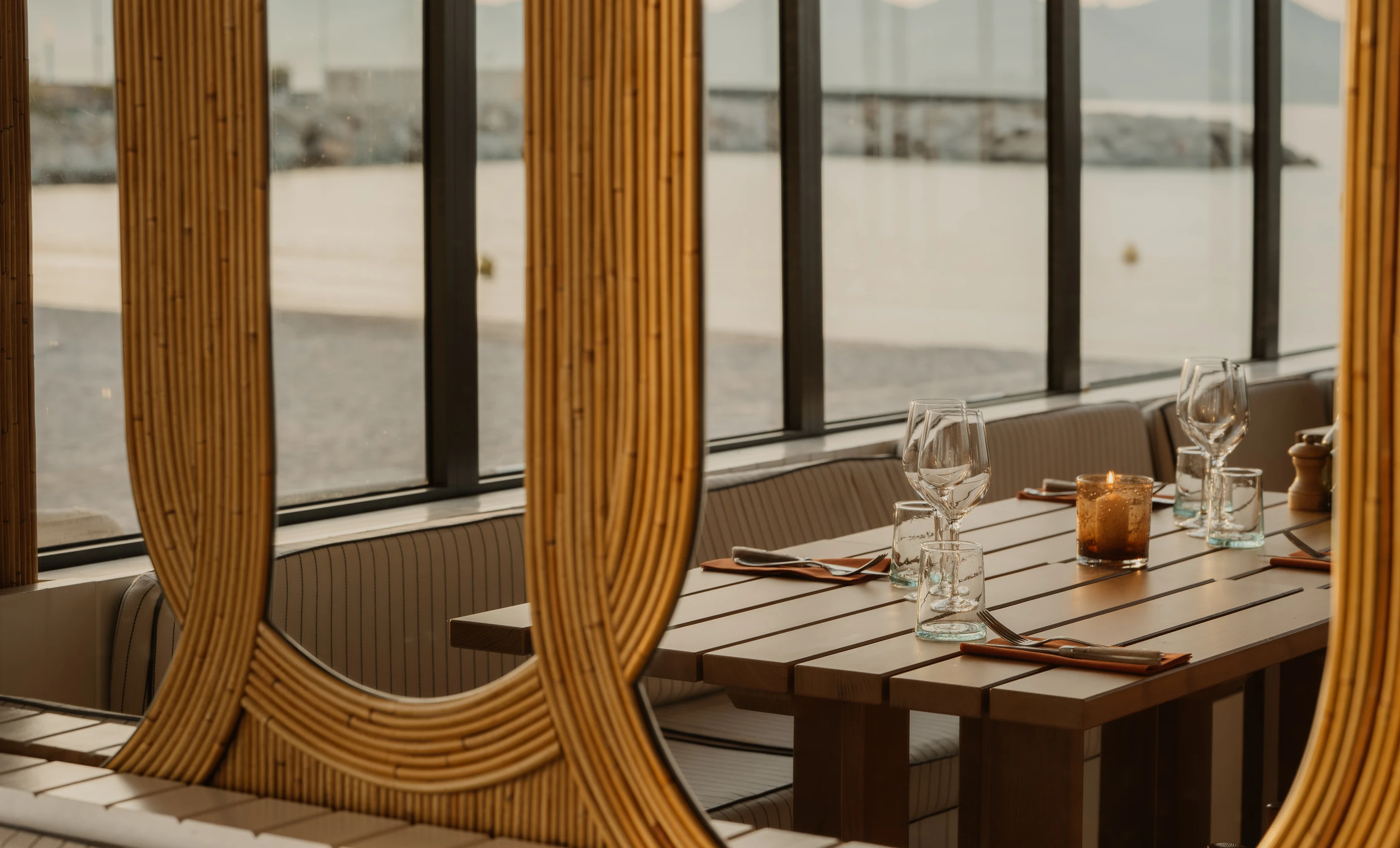 Elegant table setting inside an Experimental Group restaurant with bamboo decor and views of the sea.