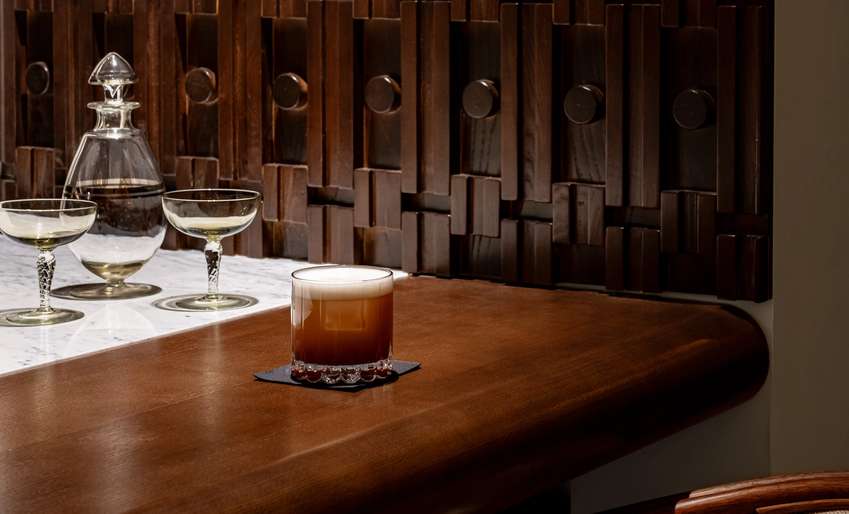 Close-up of a craft cocktail served in glassware on the bar top at the Experimental Cocktail Club, emphasizing the attention to mixology.