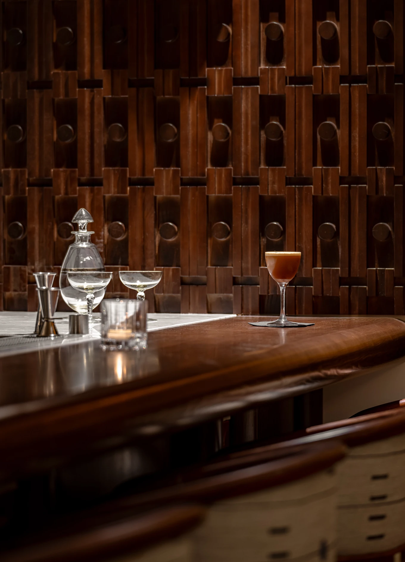 signature craft cocktail served at the wooden bar counter of the Experimental Cocktail Club, set against a detailed textured wood wall.