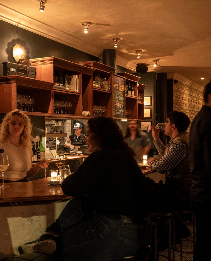 Les clients dégustent du vin et font des rencontres au bar en marbre de l'Experimental Cocktail Club, qui met en valeur l'atmosphère chaleureuse et intime.