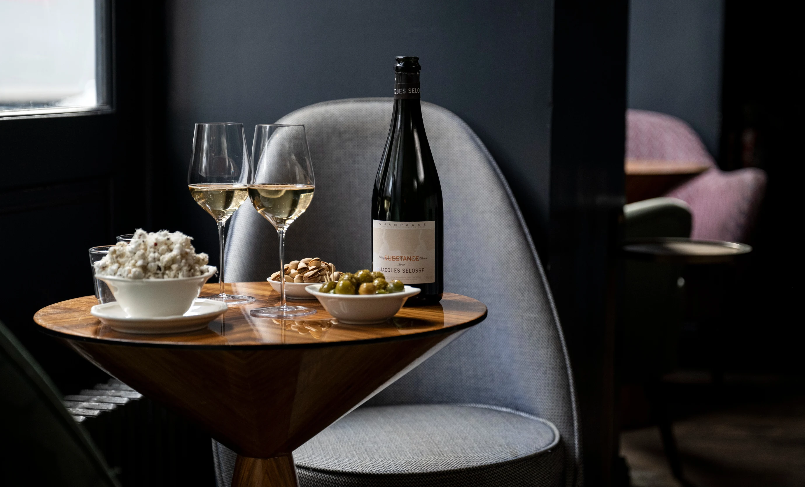 Bar table with a bottle of Jacques Selosse champagne, olives, and snacks in an Experimental Group setting.