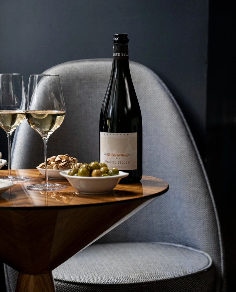 Bottle of Jacques Selosse champagne and glasses placed on a designer wooden table in an Experimental Group bar.