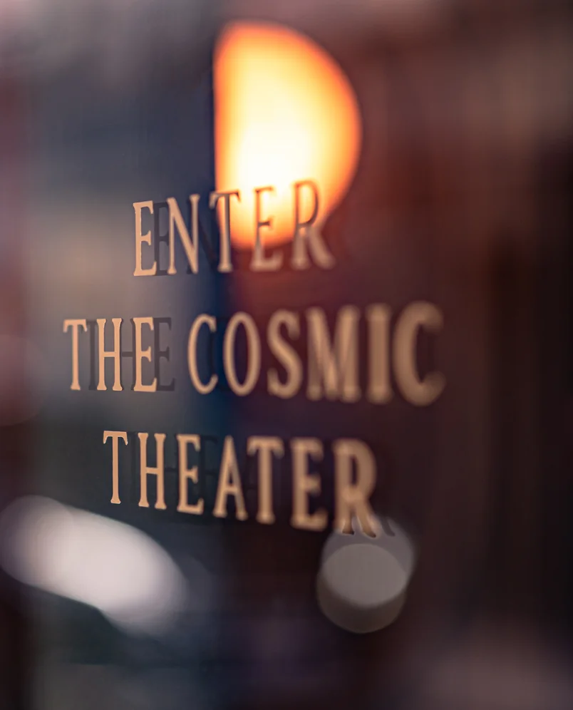"Enter the Cosmic Theater" sign glowing on a glass door at an Experimental Group establishment.