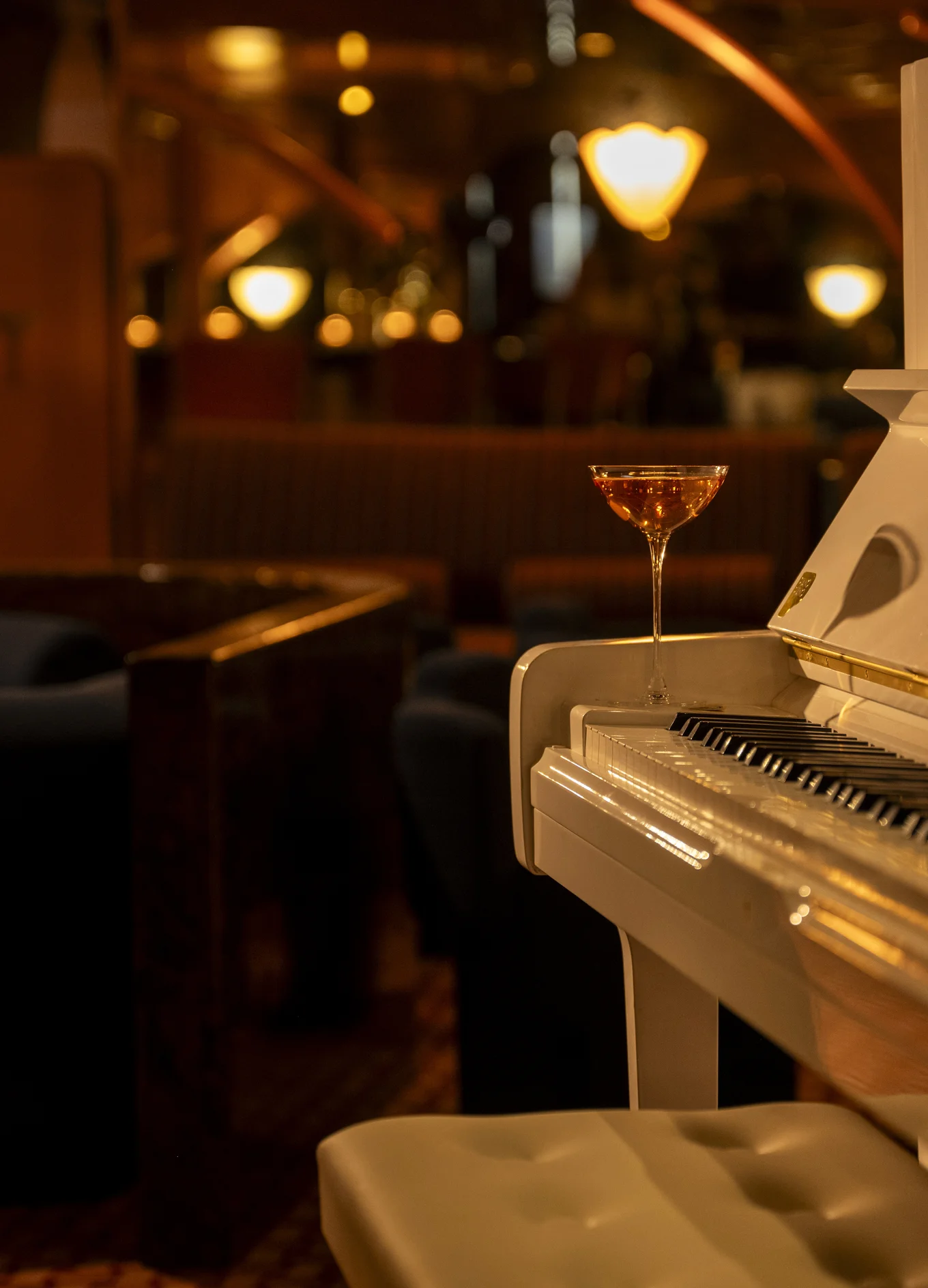 Copo de coquetel colocado em um piano de cauda branco dentro de um bar do Grupo Experimental.