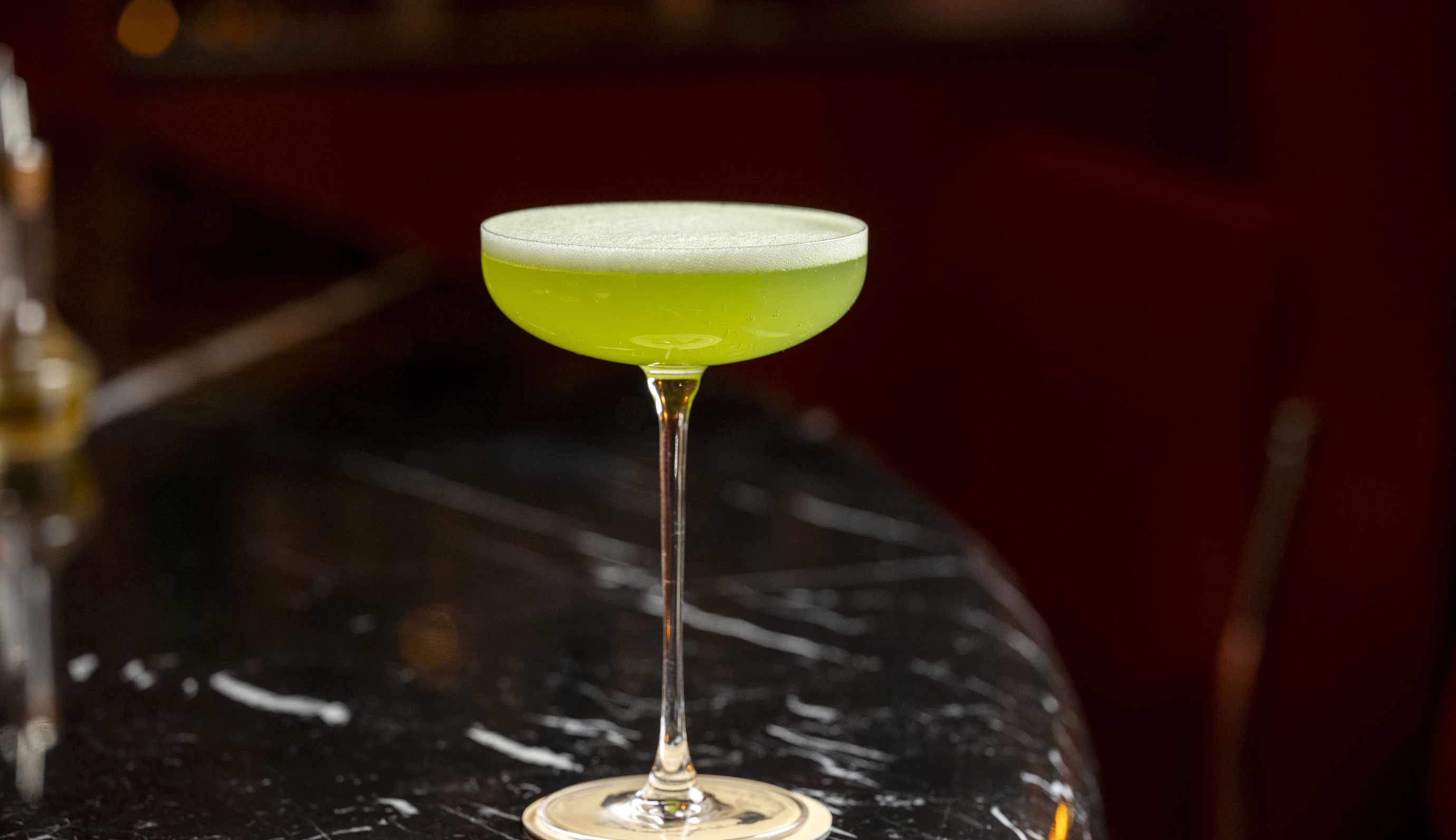 Um coquetel verde exclusivo, vibrante e habilmente elaborado em uma taça cupê, servido em um bar de coquetéis do Experimental Group.