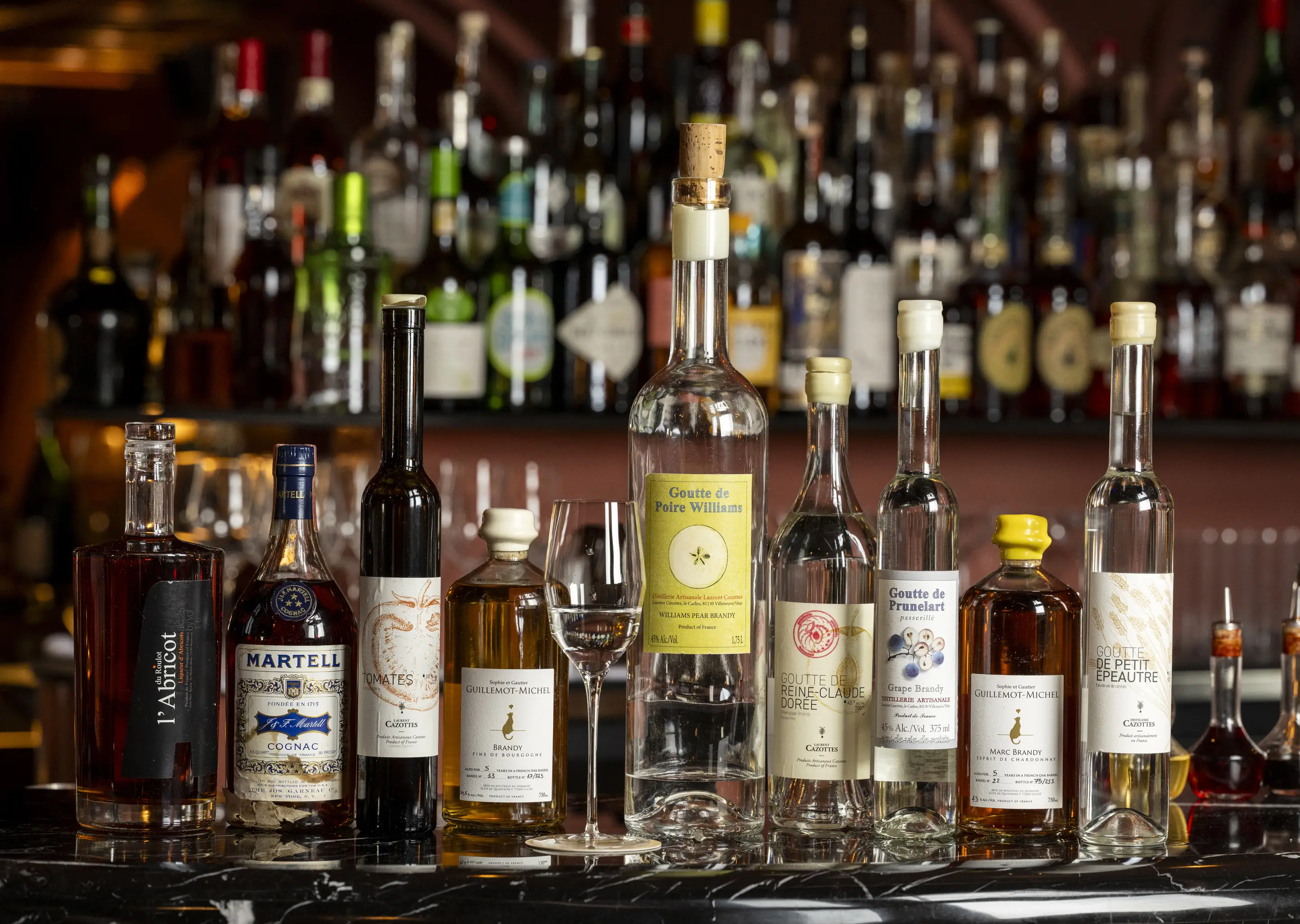 Collezione assortita di bottiglie di liquore e brandy artigianali presentate sul bancone di un bar di Experimental Group.