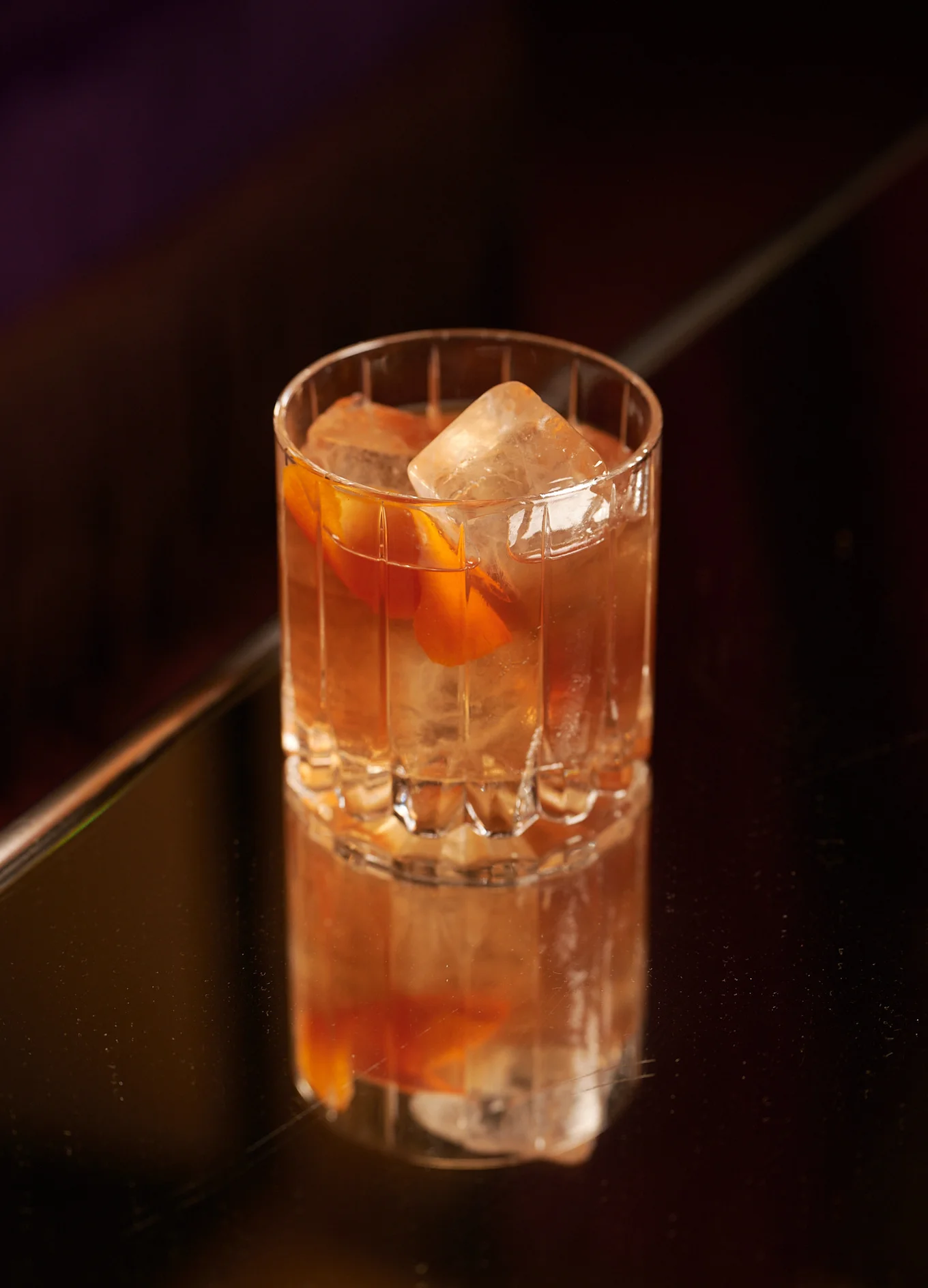 Refined cocktail in a crystal glass with ice cubes and orange peel on a dark table at the Experimental Group.
