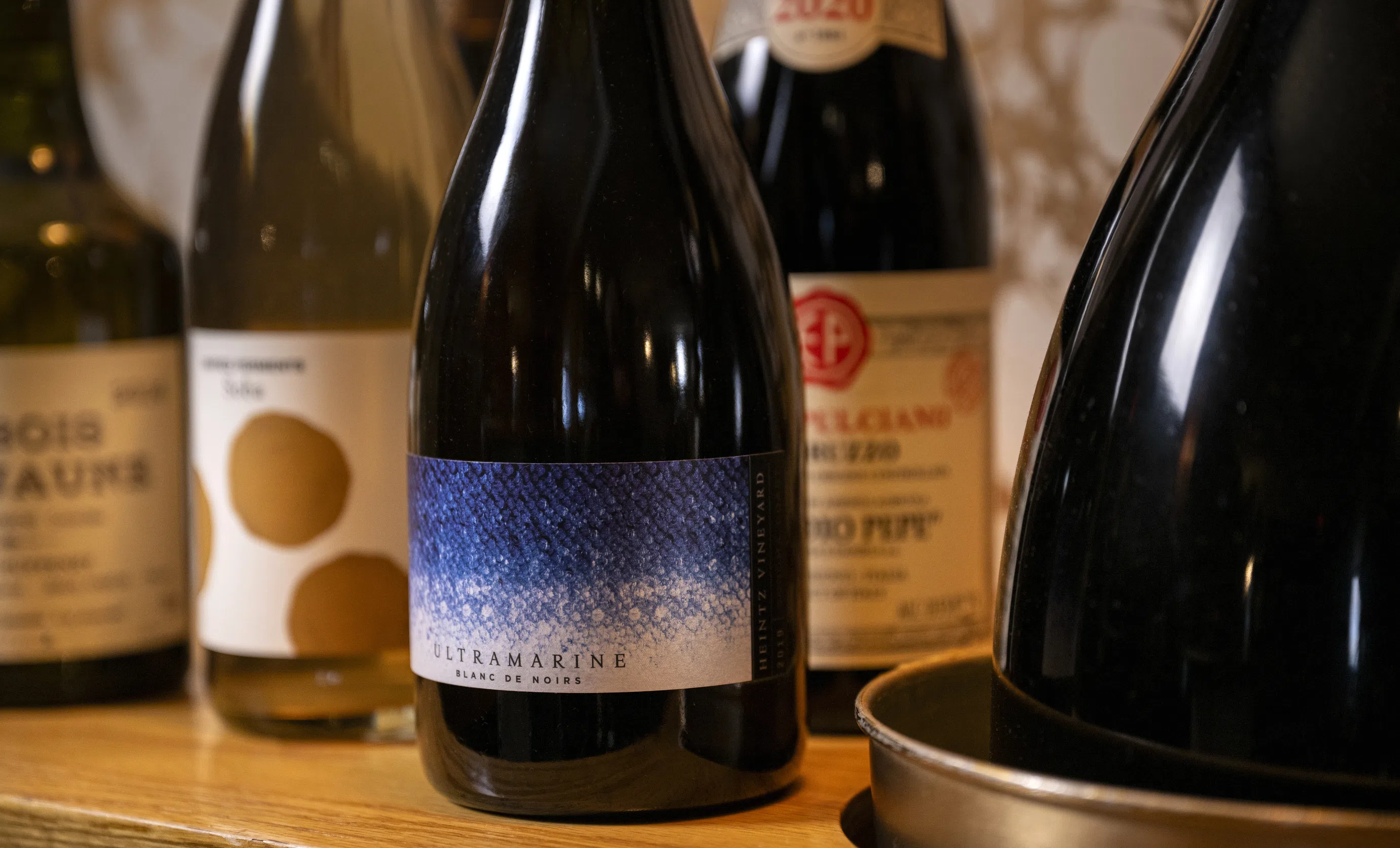 Close-up of premium wine bottles, including an Ultramarine Blanc de Noirs, in an Experimental Group wine cellar.