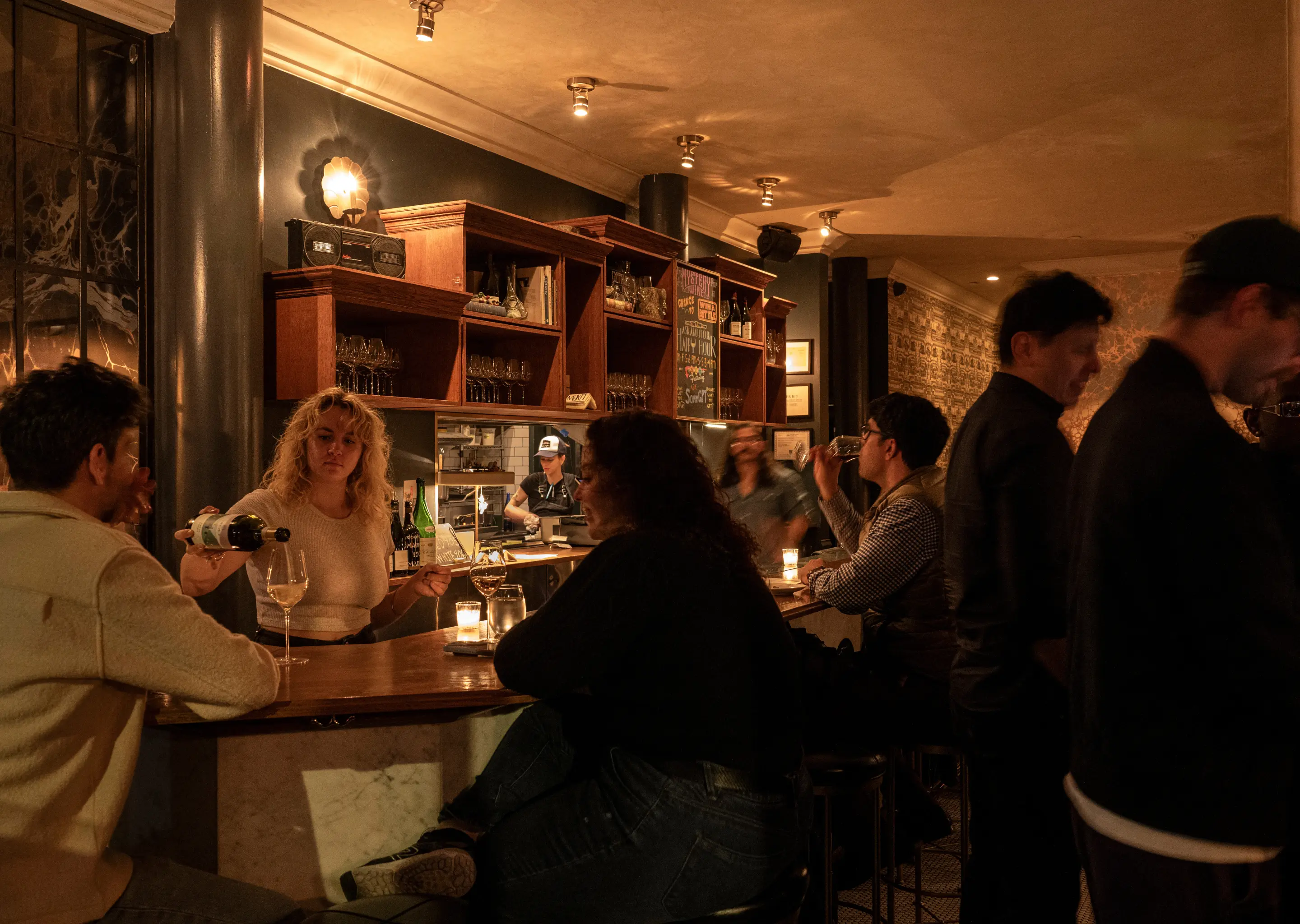 Customers sitting at the marble bar of The Henrietta Hotel, featuring a bartender, wine bottles, and neon signage.