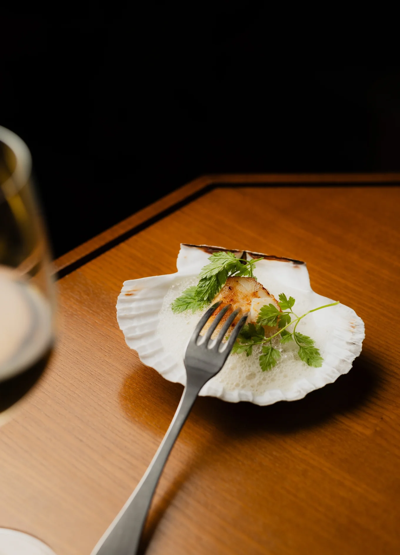 Pan-seared scallop with light foam and herbs, served in a shell on a wooden table at The Henrietta Hotel.