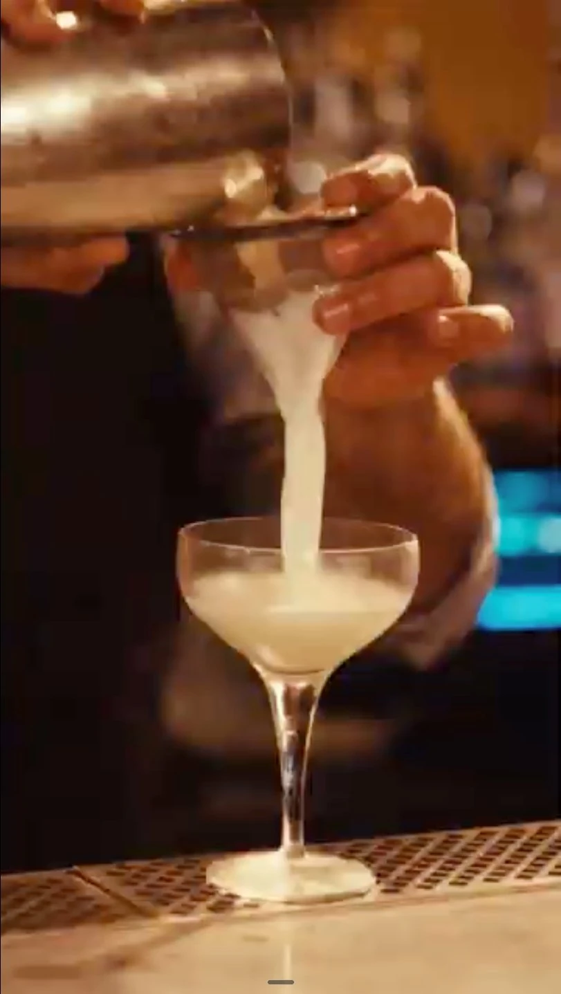 Strained cocktail being poured into a coupe glass at the bar of The Henrietta Hotel, London.