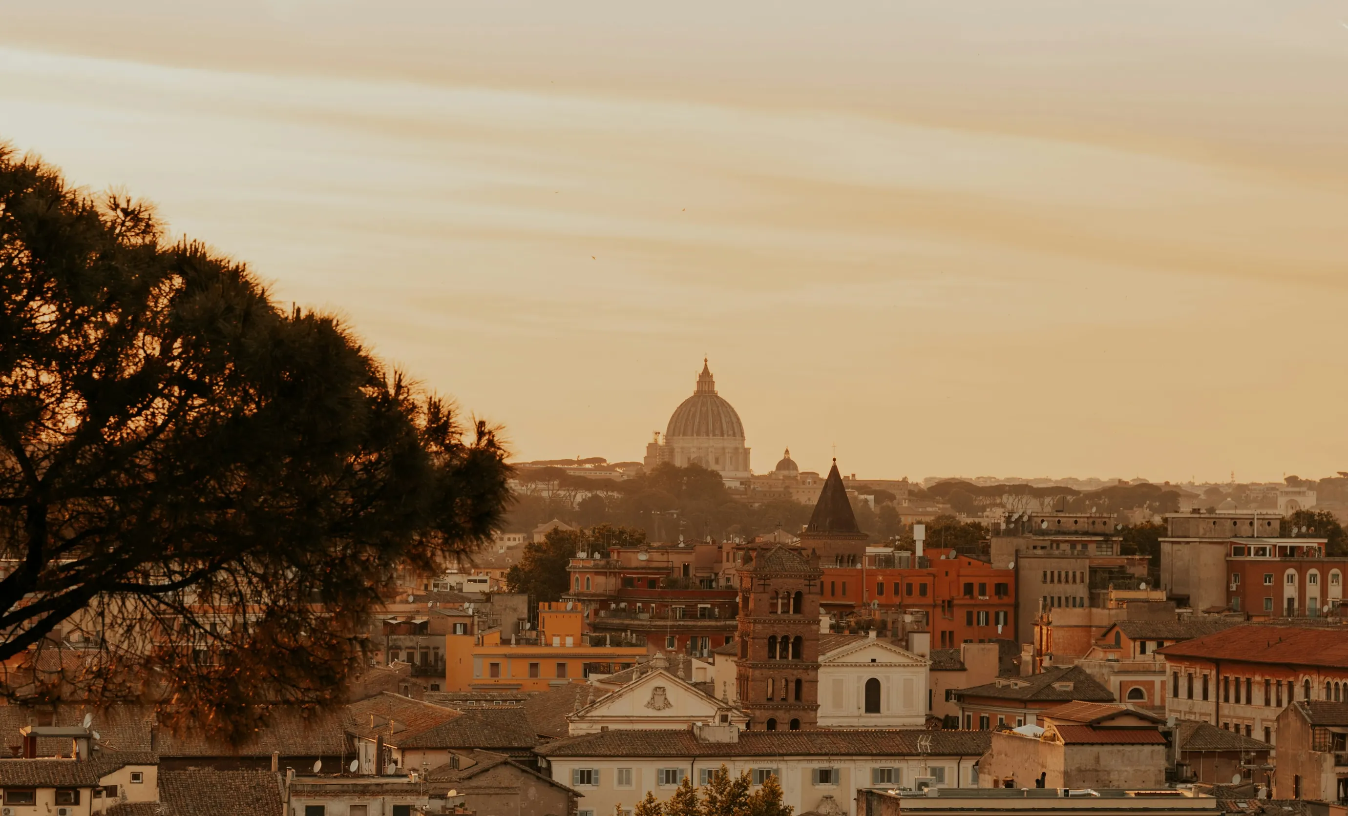 Vista panoramica al tramonto sui tetti di Roma, con la cupola della Basilica di San Pietro sullo sfondo.
