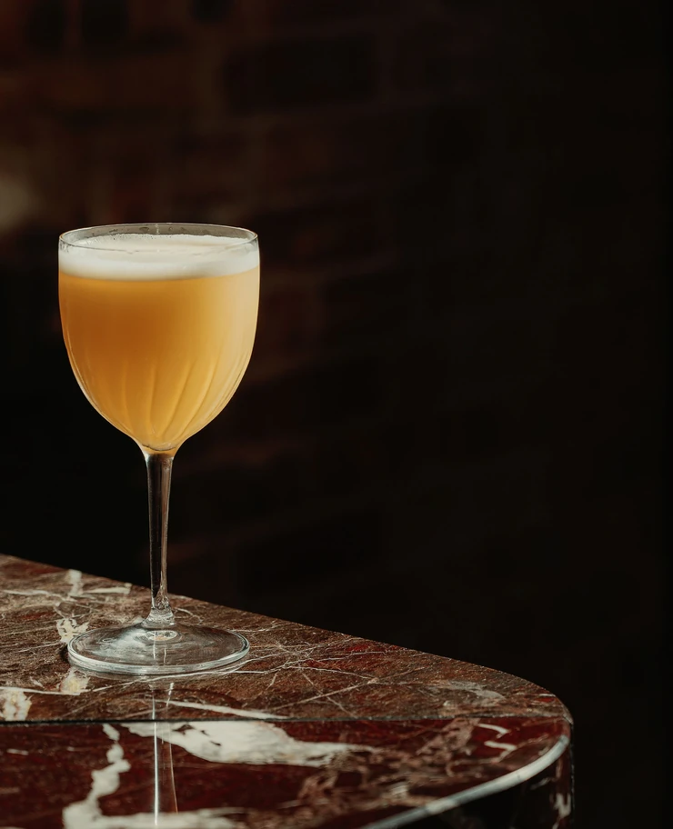 Vue détaillée d'un cocktail jaune mousseux et rafraîchissant dans un verre de style vintage dans un bar Experimental Group.