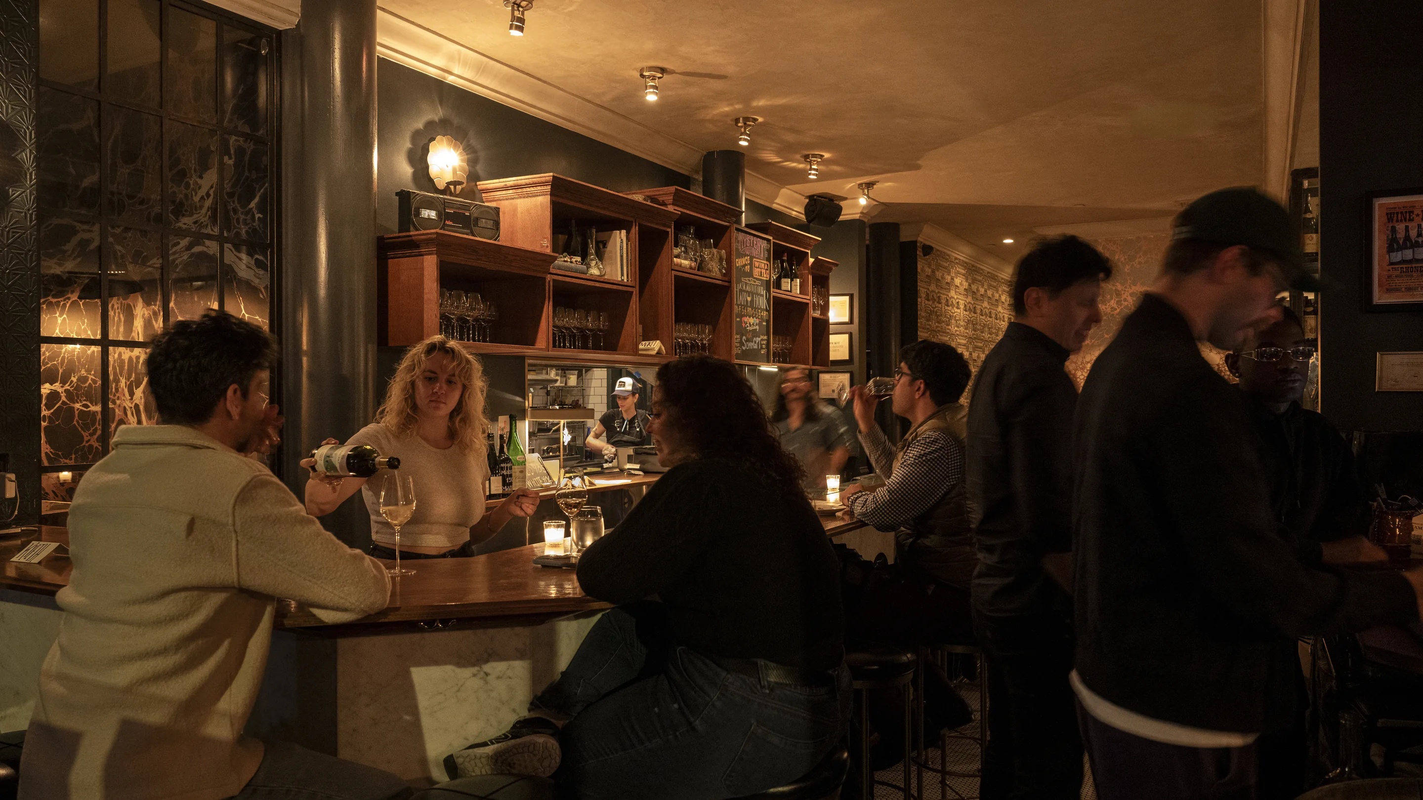 Wide shot of a lively Experimental Group bar atmosphere, with customers interacting at the counter and professional service staff.