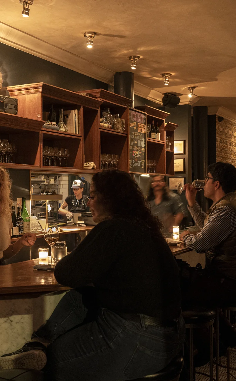 Guests socializing at the marble bar counter of an Experimental Group establishment, enjoying premium cocktails and wine.