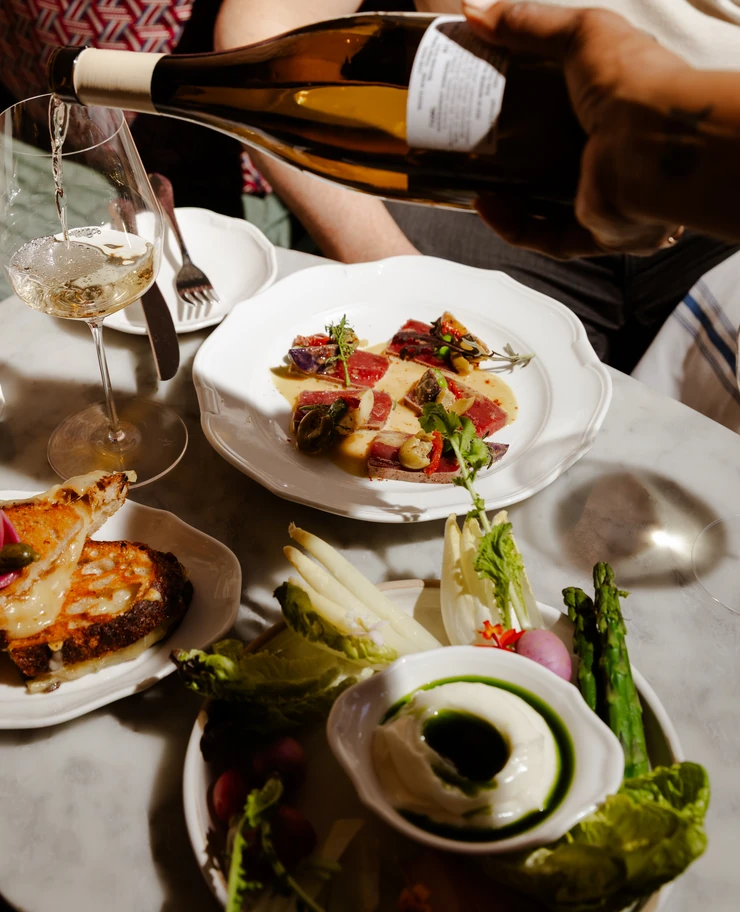 High-end dining experience at an Experimental Group restaurant, showing white wine being poured over a gourmet meal.