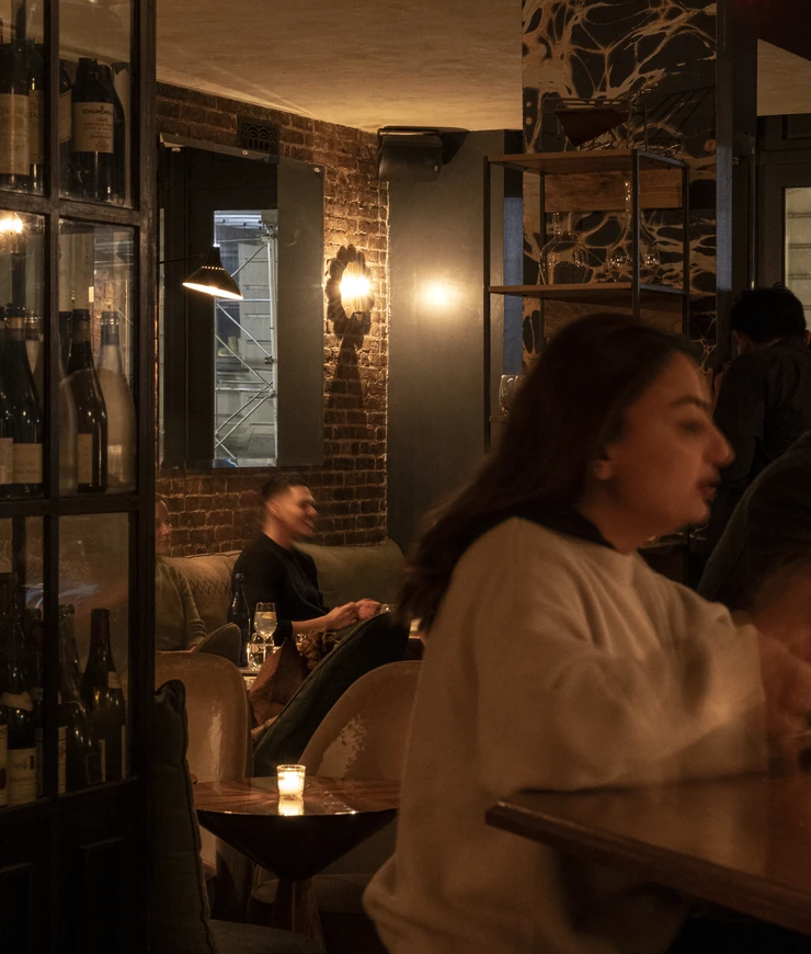 Intimate evening scene at an Experimental Group cocktail bar in London, showing patrons relaxing in a stylish, brick-walled environment.