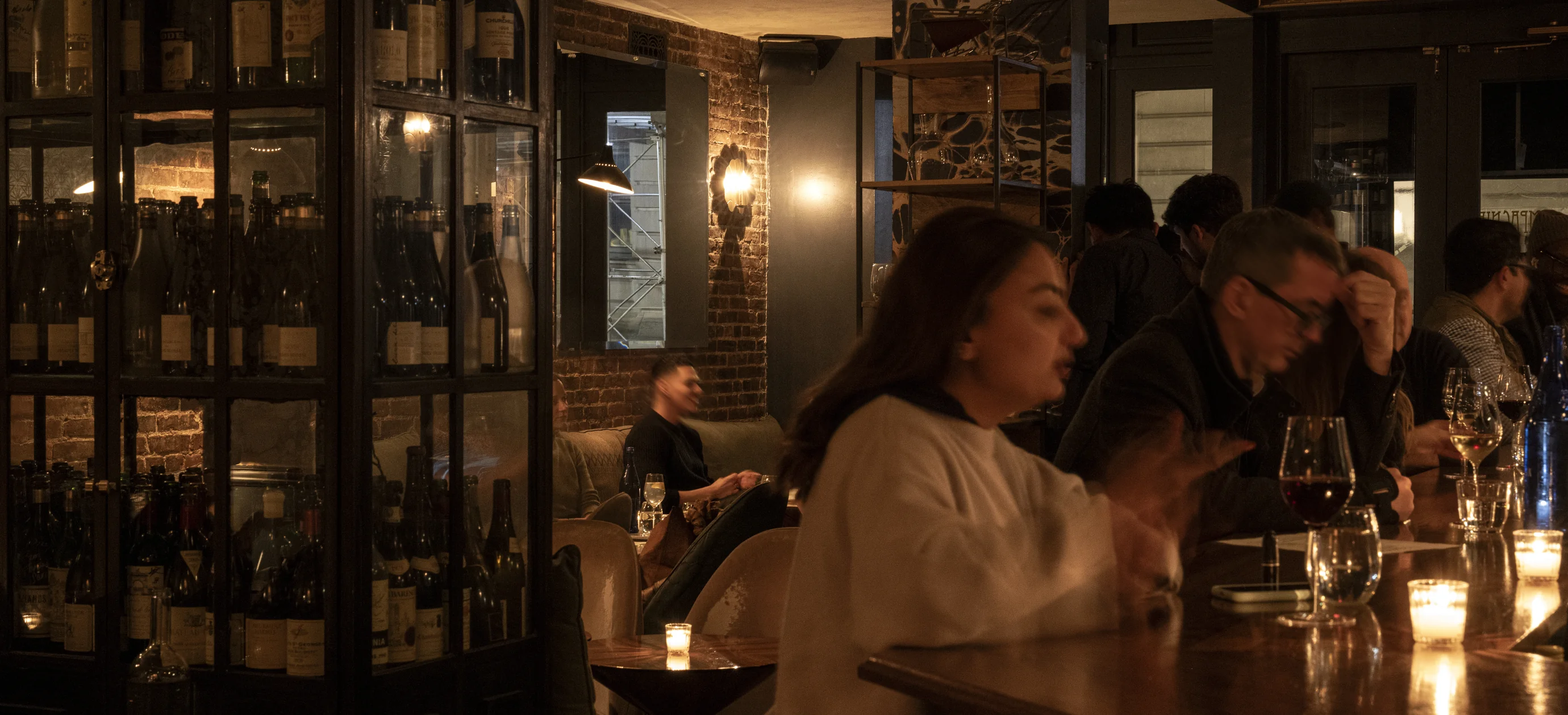 Guests enjoying a drink at the wooden bar counter of an Experimental Group venue, featuring a warm and intimate atmosphere in London.