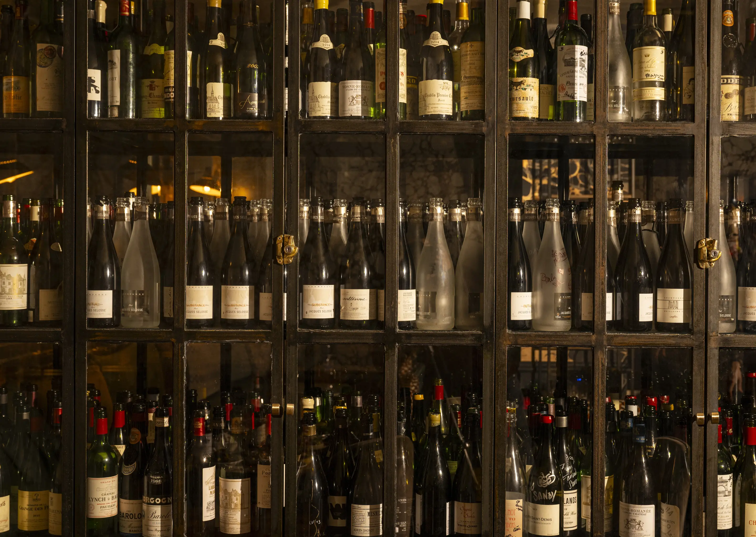 Extensive collection of fine wines and champagnes stored in an industrial-style display case at an Experimental Group bar.