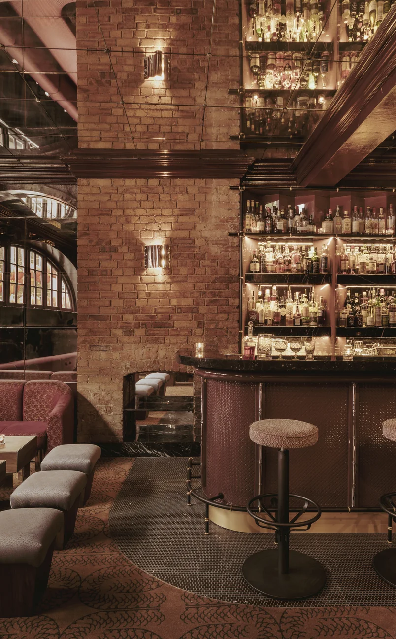Gros plan d'un mur de briques et d'un comptoir de bar bien approvisionné dans un établissement d'Experimental Group, mettant en valeur un design d'intérieur sophistiqué.