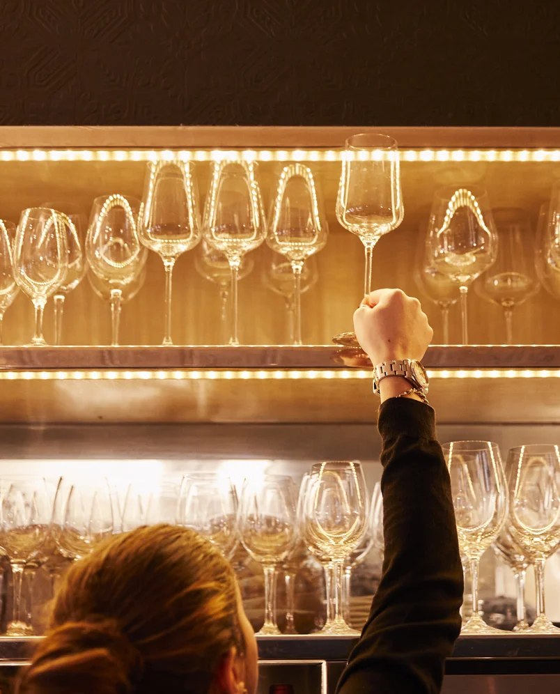 A hand grabbing a wine glass from a glowing shelf, the art of hospitality at Experimental Group.