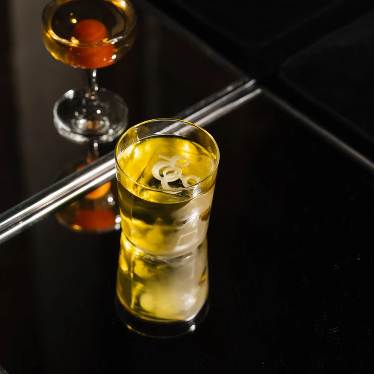 Close-up view of a clear artisanal cocktail and its reflection on a glossy black surface in an Experimental Group venue.