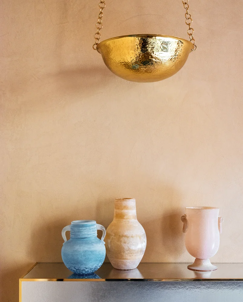 Close-up of colored glass vases positioned beneath a golden light fixture at Palazzo Experimental, Venice.
