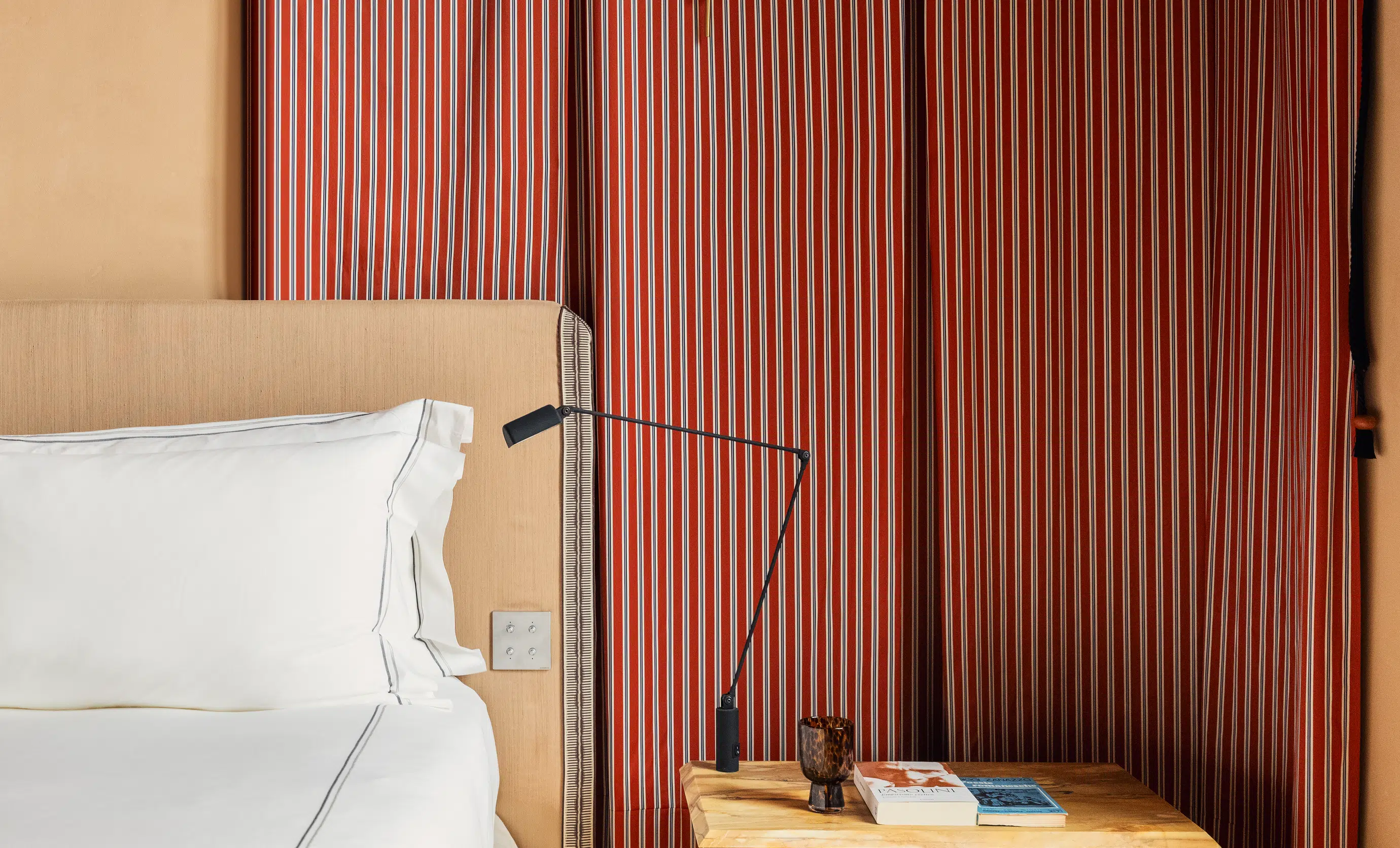 Detail of a bedroom interior with striped curtains, reading lamp, and wooden nightstand at Palazzo Experimental, Venice.