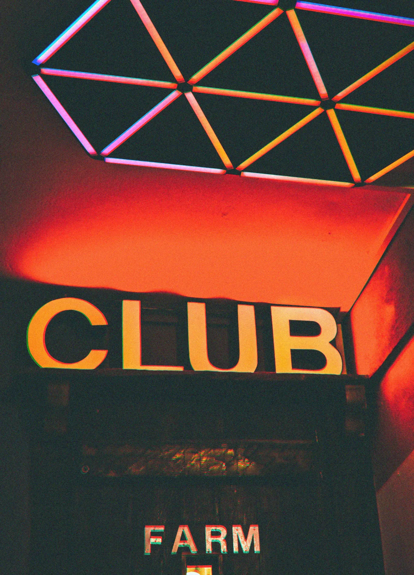 Cartel de neón que muestra la palabra «CLUB» debajo de un techo geométrico con retroiluminación vibrante y colorida.