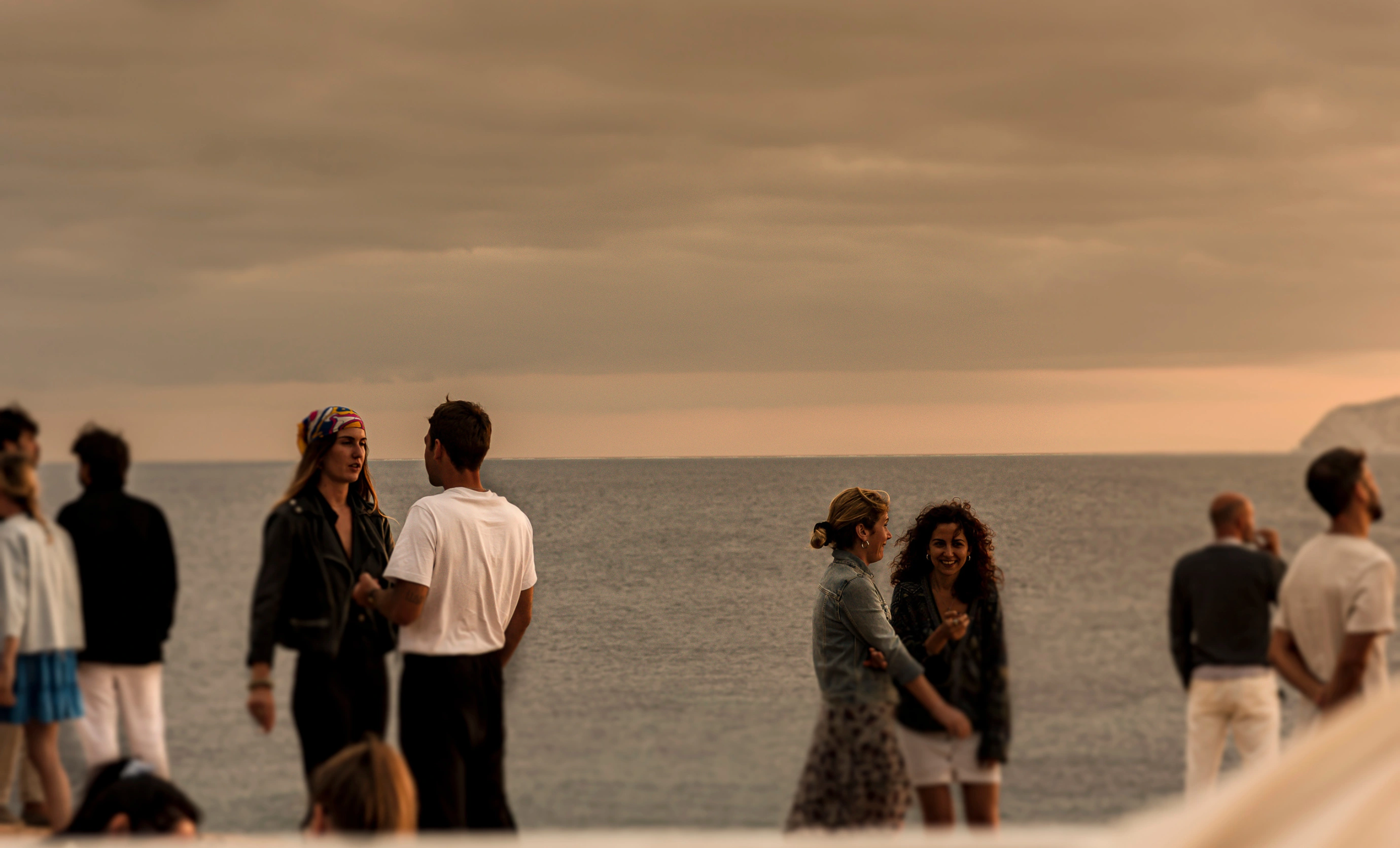Gruppo di persone che chiacchierano in riva al mare durante un tramonto, atmosfera rilassata e amichevole.