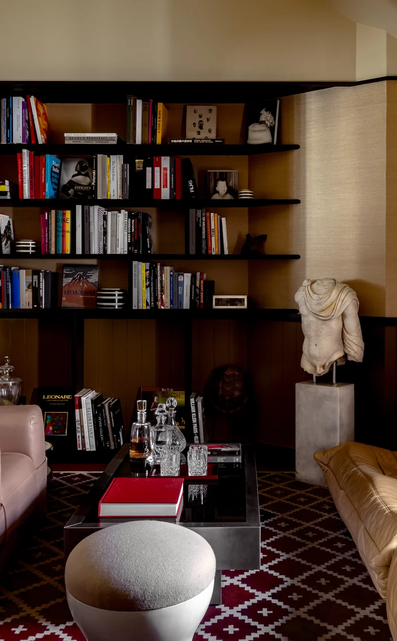 Salon confortable avec des étagères, une statue en marbre sans tête, un tabouret rond, une table basse et un canapé en cuir.