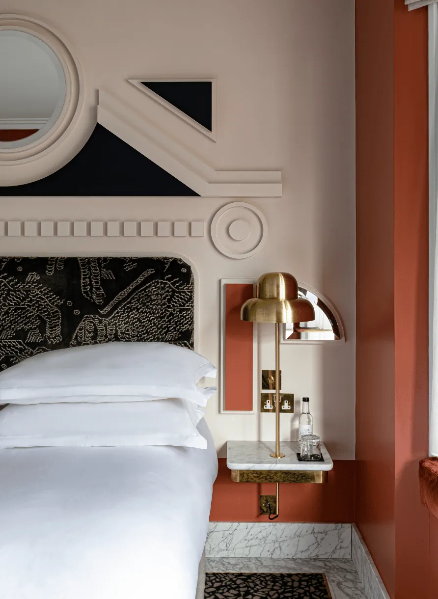 Moderno angolo della camera da letto con letto bianco, testiera nera con motivi geometrici, lampada in ottone e decorazioni murali geometriche.