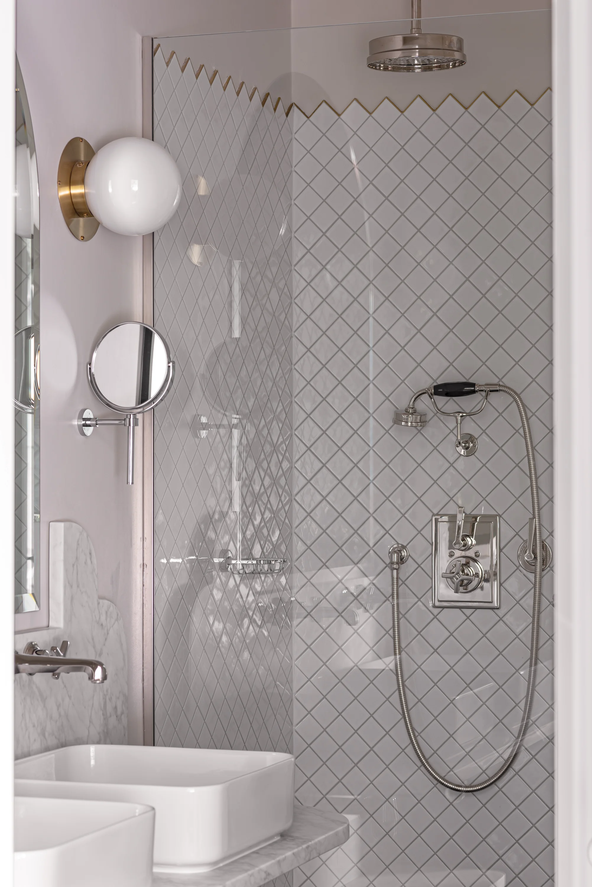 Modern bathroom with white square sink, marble countertop, tiled shower, and round wall mirror.
