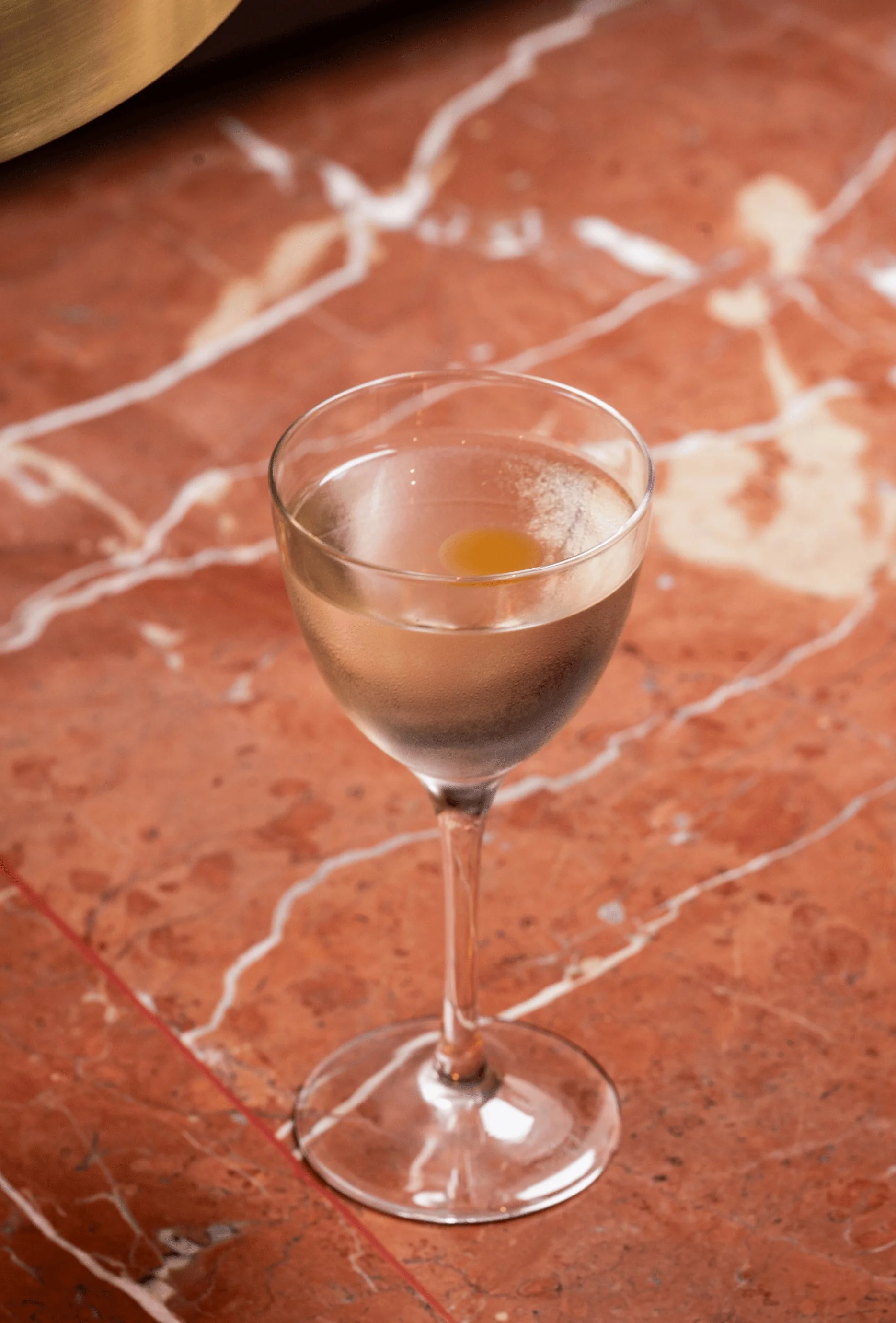 Bicchiere da cocktail con una bevanda fredda trasparente e una piccola guarnizione gialla su una superficie di marmo.