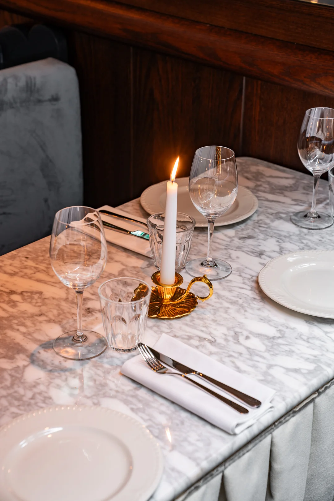 Table set with white plates, wine glasses, silverware, and a lit candle in a gold holder.