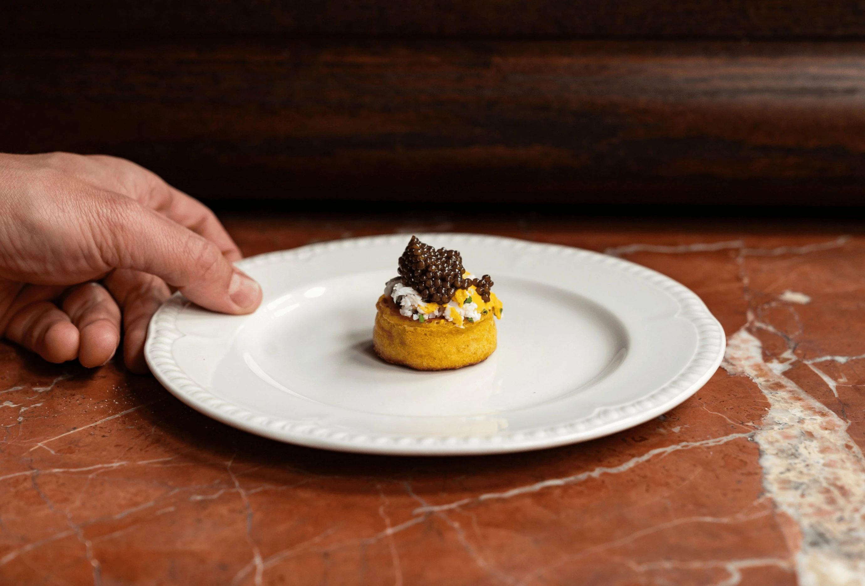 Tenendo in mano un piatto bianco con un piccolo antipasto gourmet condito con caviale su una superficie di marmo.