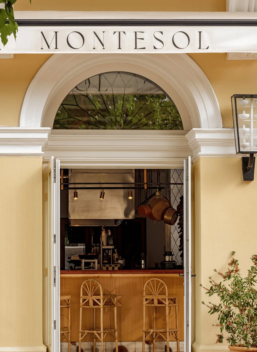 Ingresso all'hotel Montesol con porte aperte che mostrano sgabelli da bar in legno e pentole appese in rame.