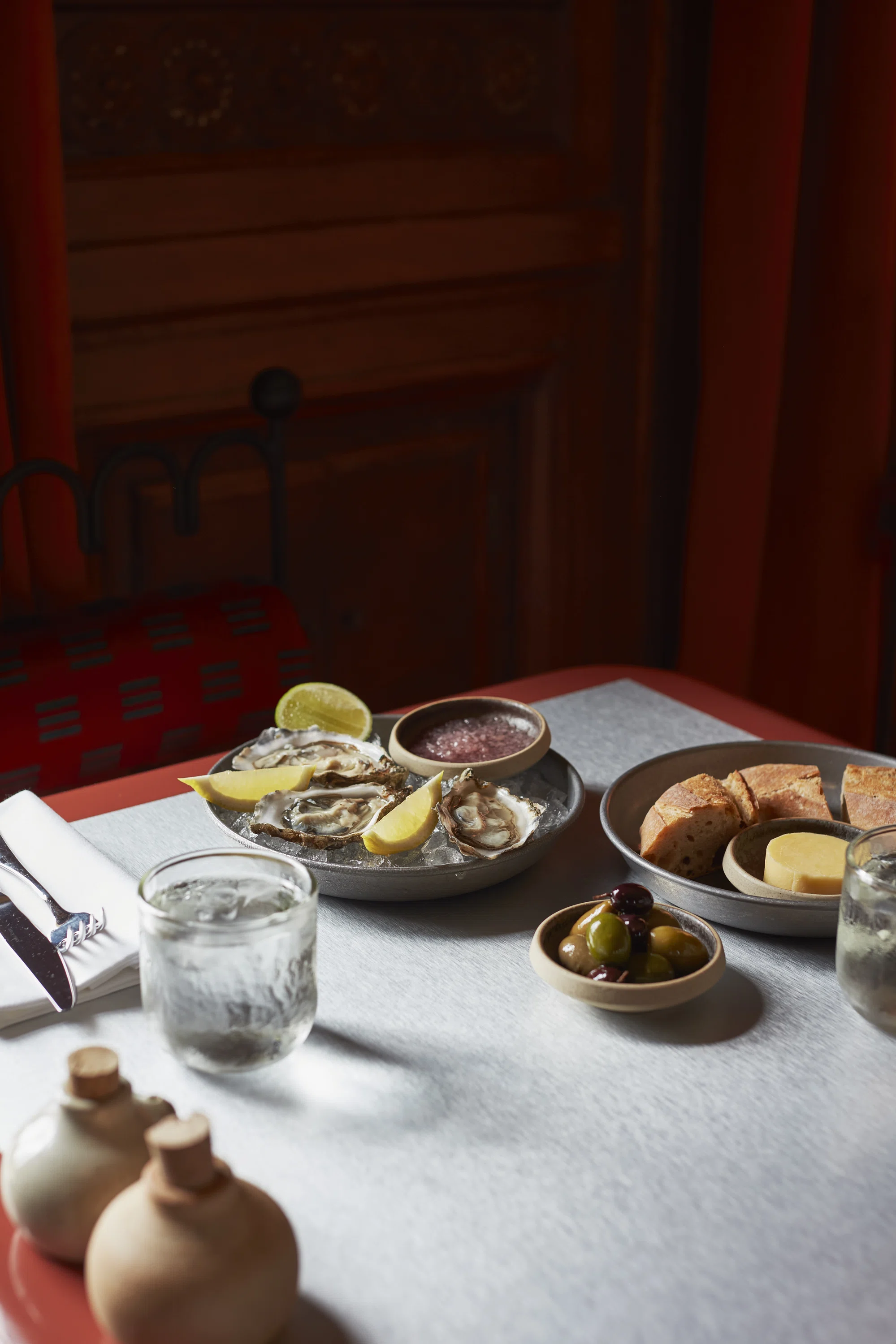 Tavolo con ostriche ghiacciate, spicchi di limone, olive, pane, burro e bicchieri d'acqua.