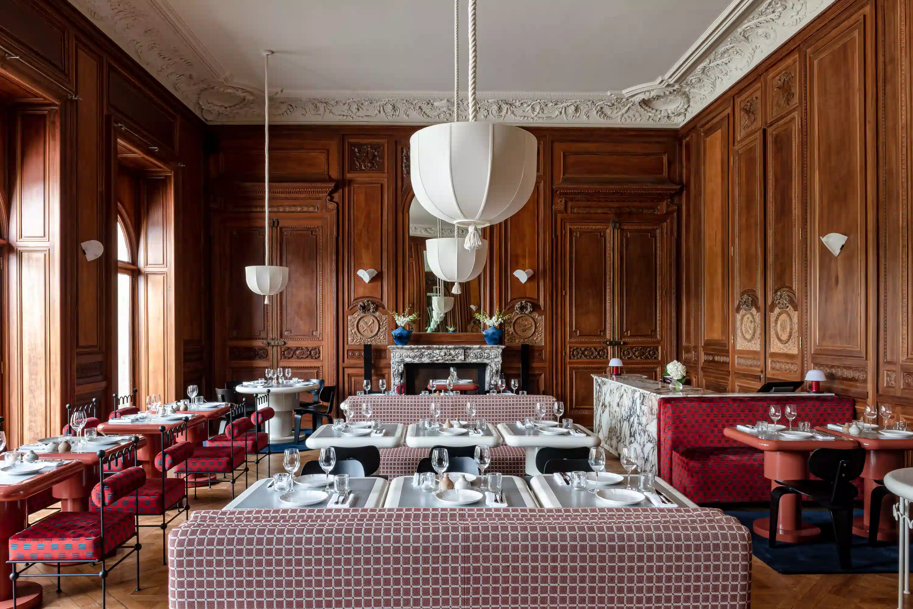 Ristorante elegante con pareti rivestite in legno, posti a sedere a motivi geometrici, tavoli bianchi e grandi lampade a sospensione.