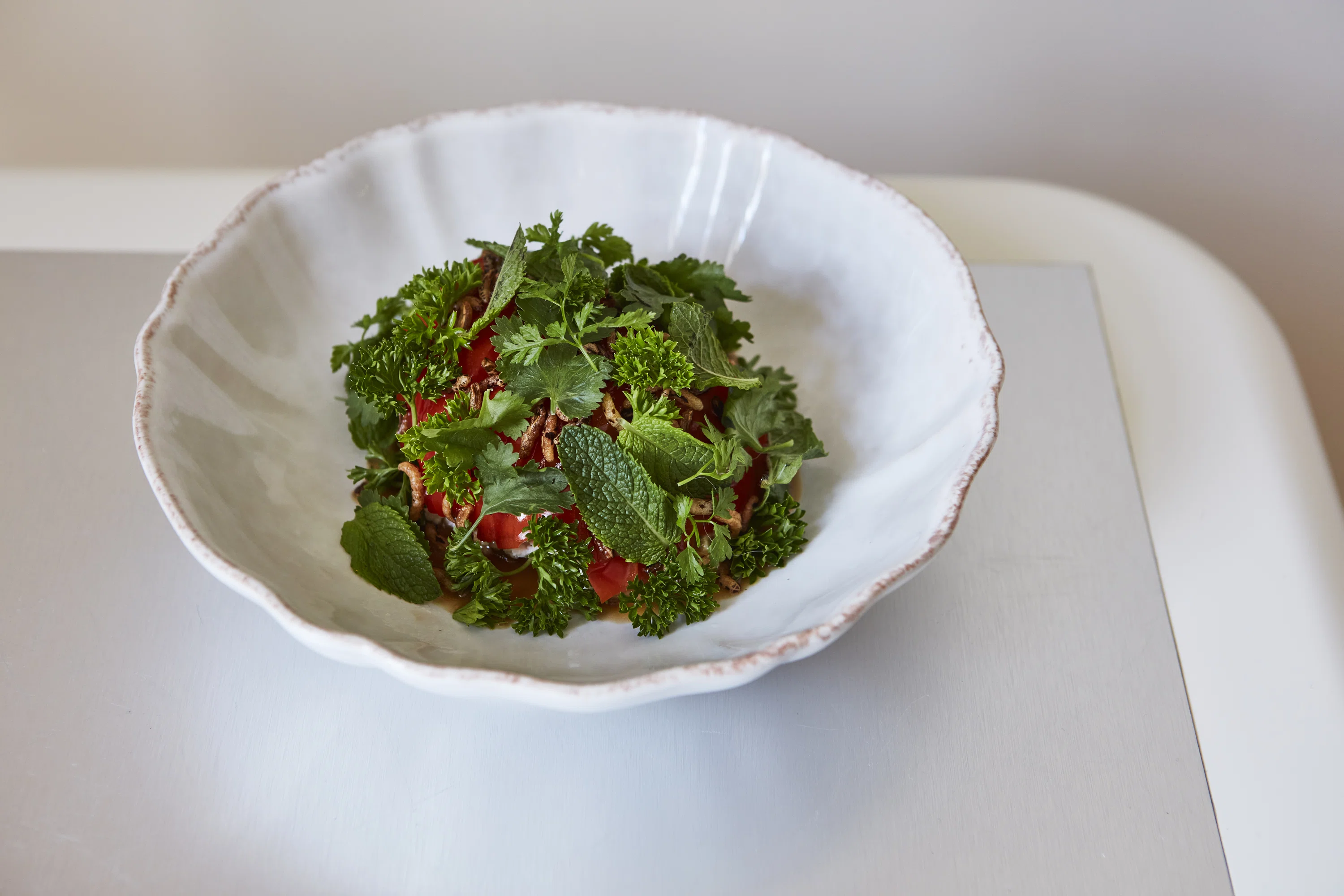 Ciotola in ceramica bianca con un piatto di pomodoro condito con erbe verdi fresche e scalogno croccante.