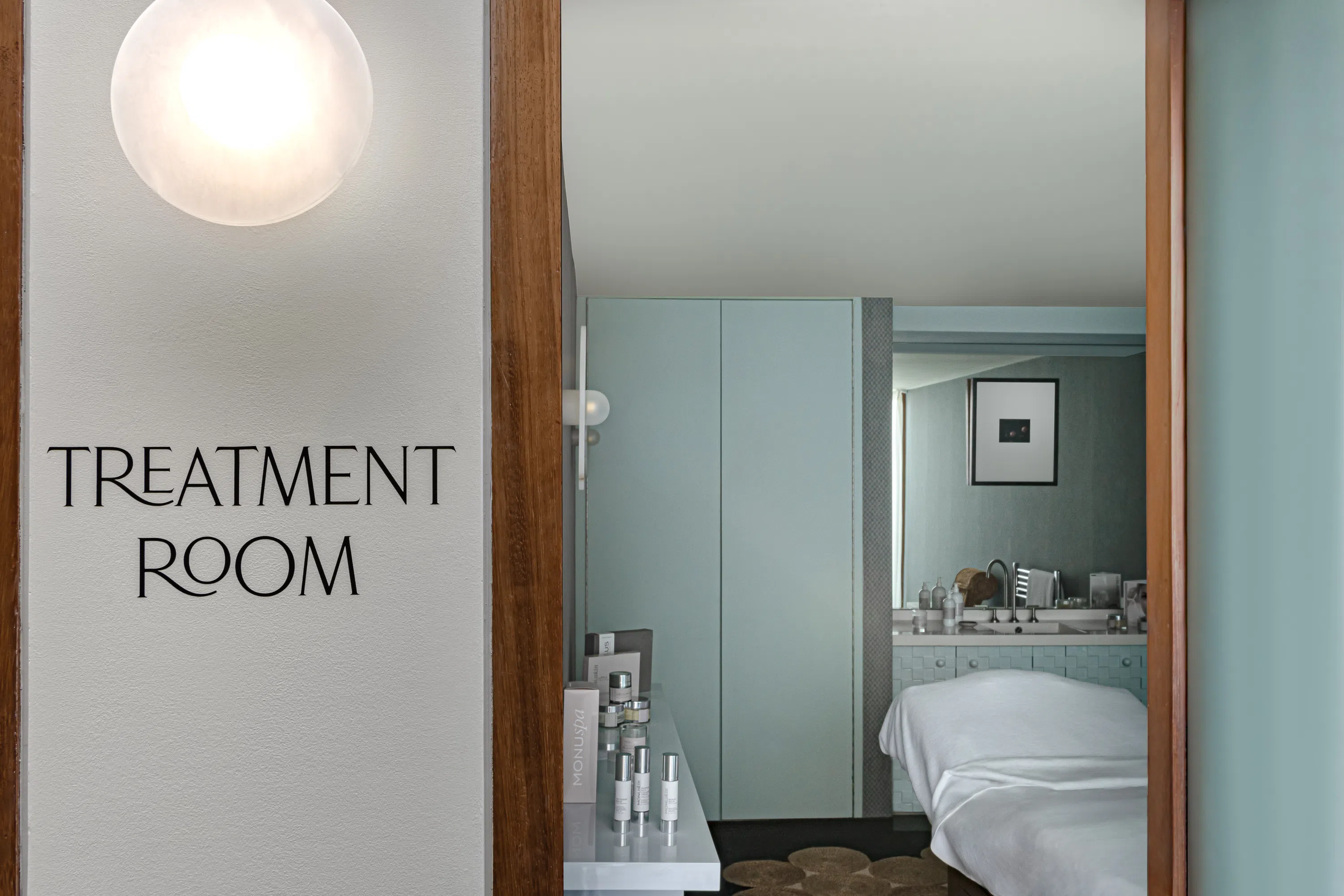Sala trattamenti con lettino da massaggio, prodotti per la cura della pelle su un lettino, luci soffuse e un quadro incorniciato sul muro.