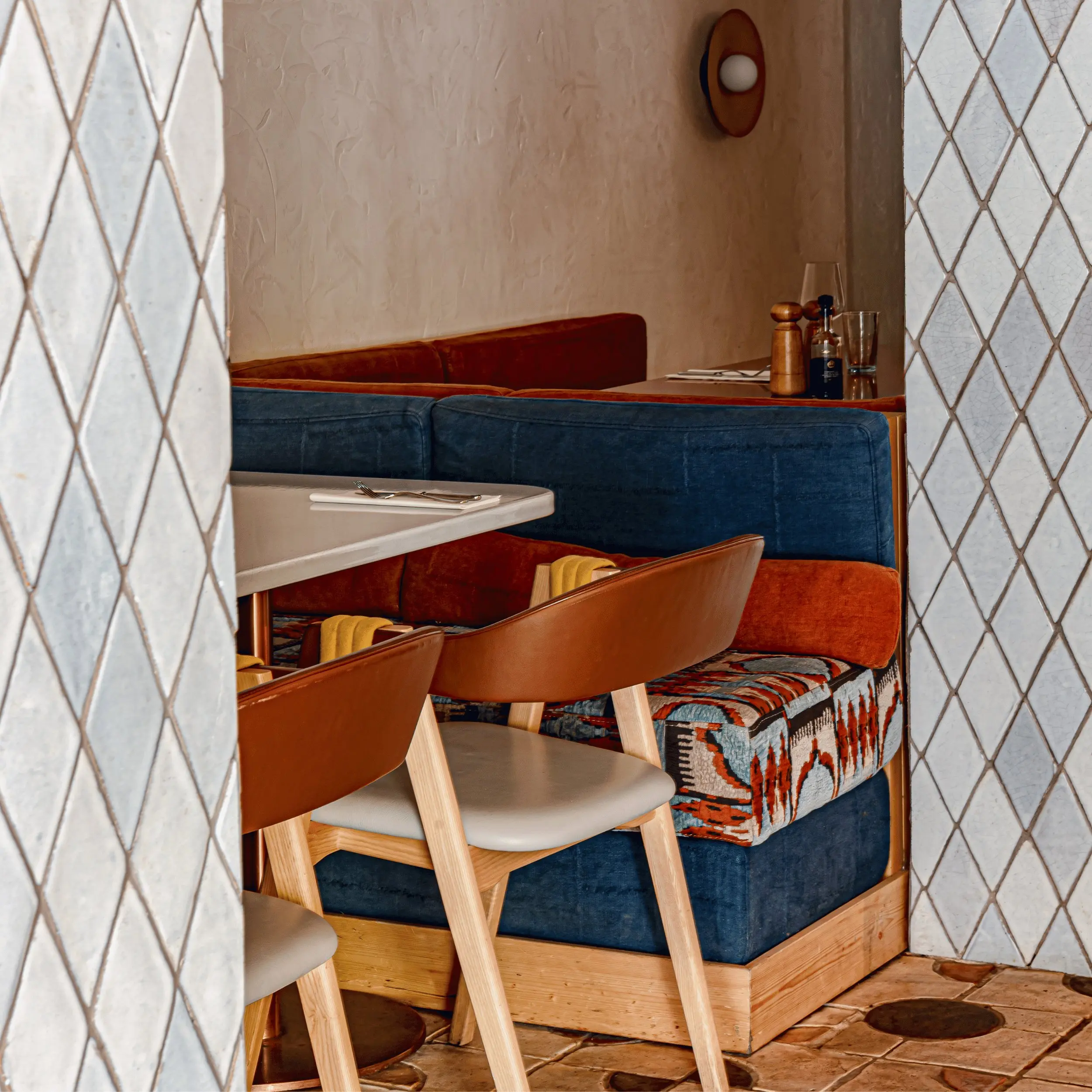 Cozy restaurant corner with blue and orange cushioned bench and wooden chairs at a table.