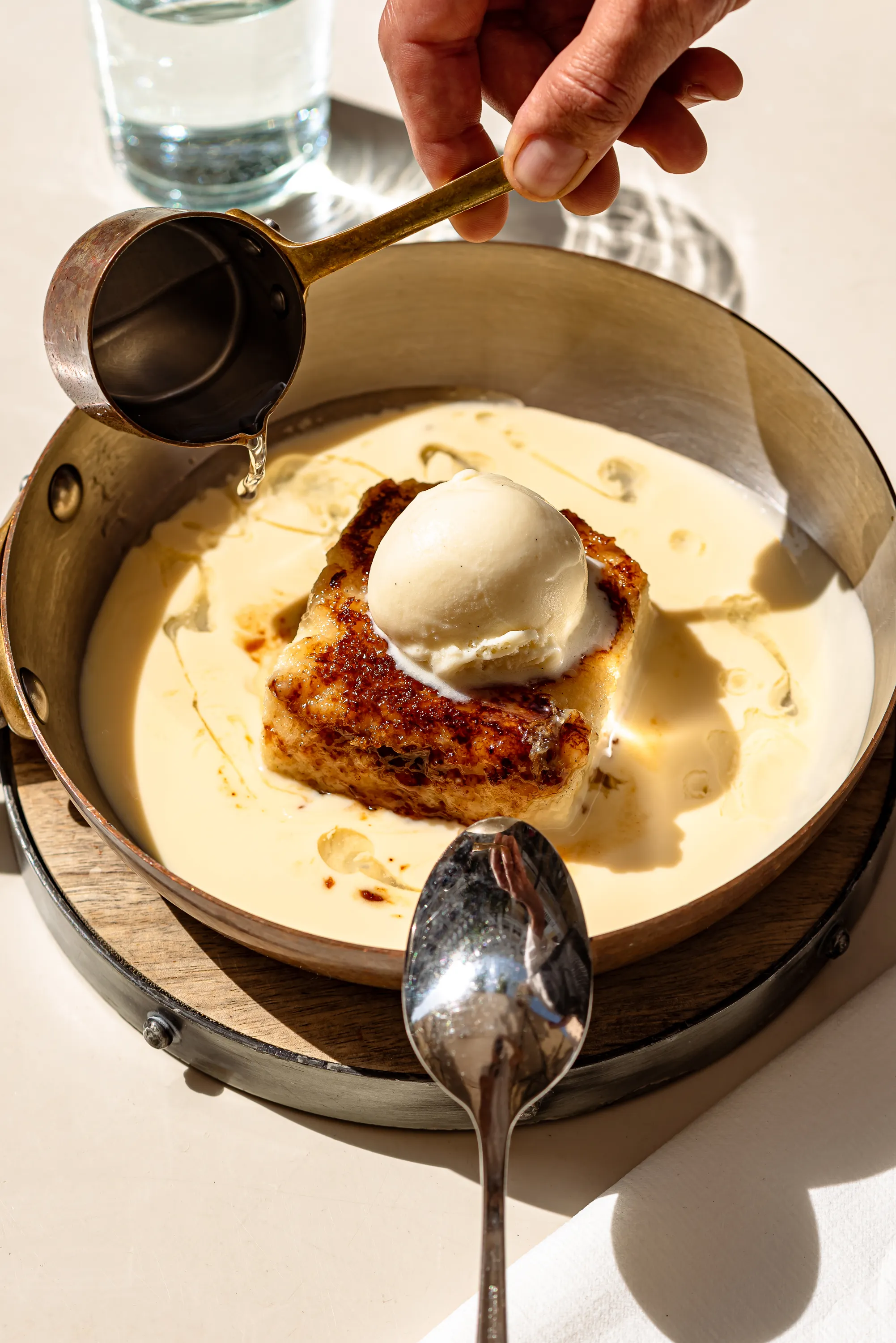 Servire la salsa sul dessert condita con gelato in una padella di metallo con un cucchiaio accanto.