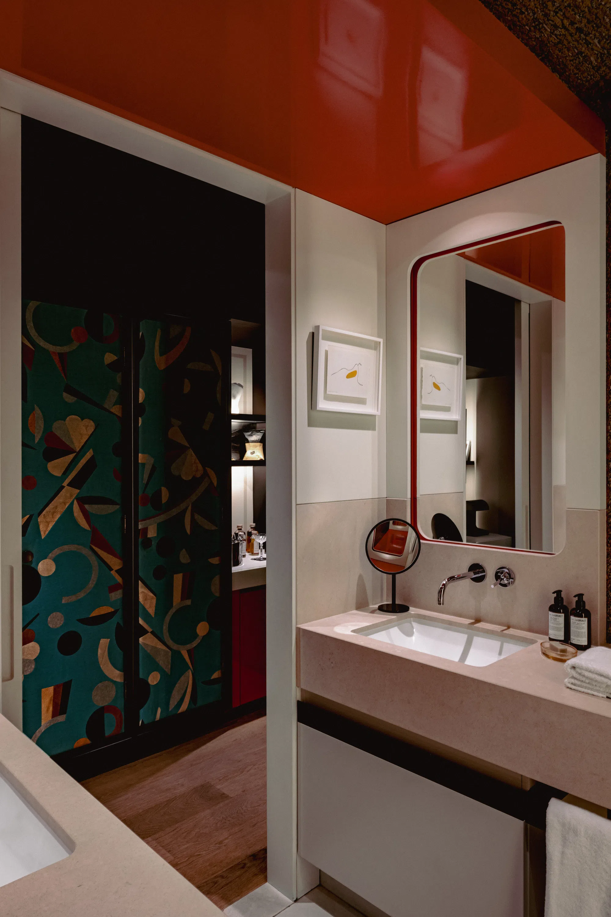 Baño moderno con una encimera de lavabo de color beige, un espejo redondo y un armario con motivos abstractos en el fondo.