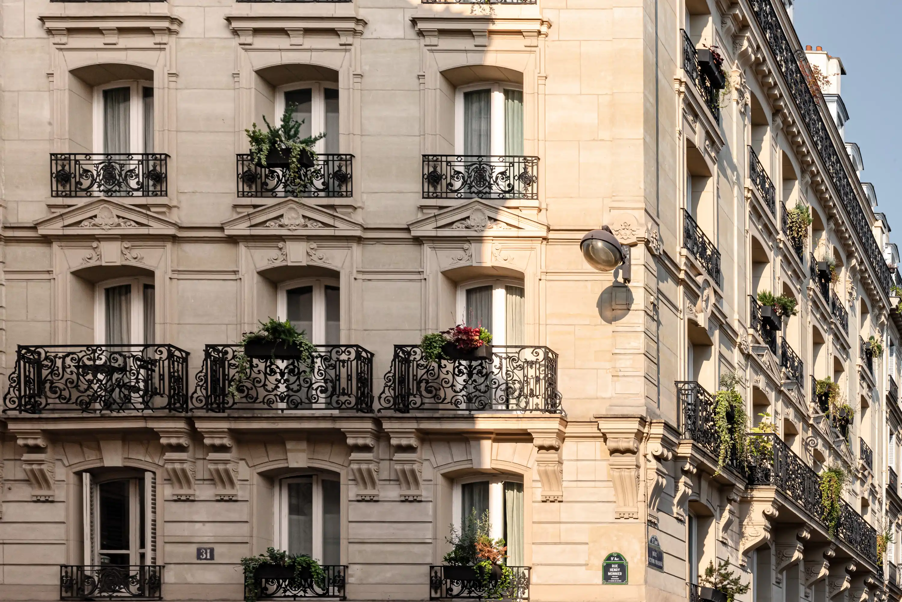 Classico edificio parigino beige con balconi decorati in ferro nero e piante su di essi.