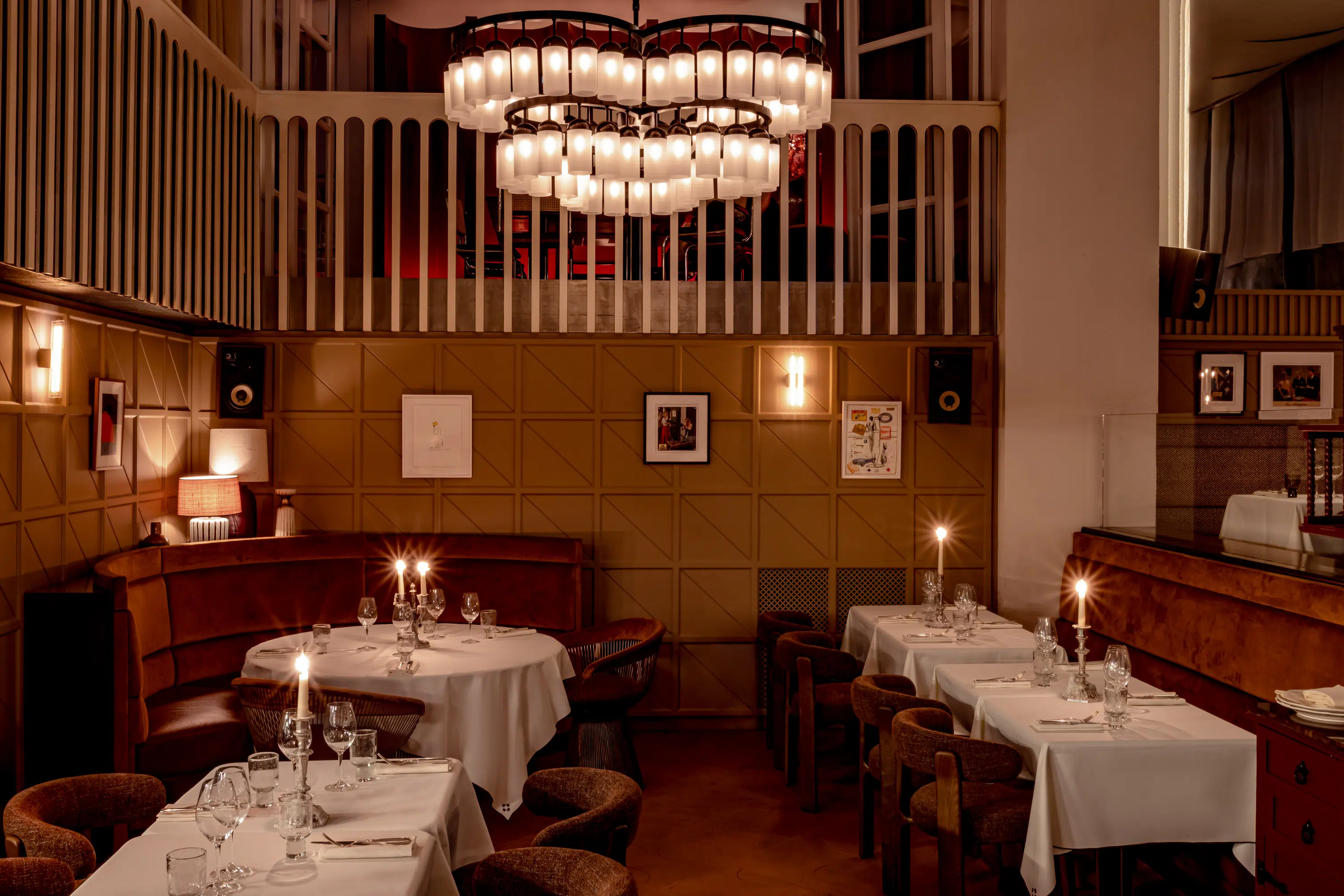Elegante interior de restaurante con mesas redondas y cuadradas, manteles blancos, velas y una iluminación cálida.