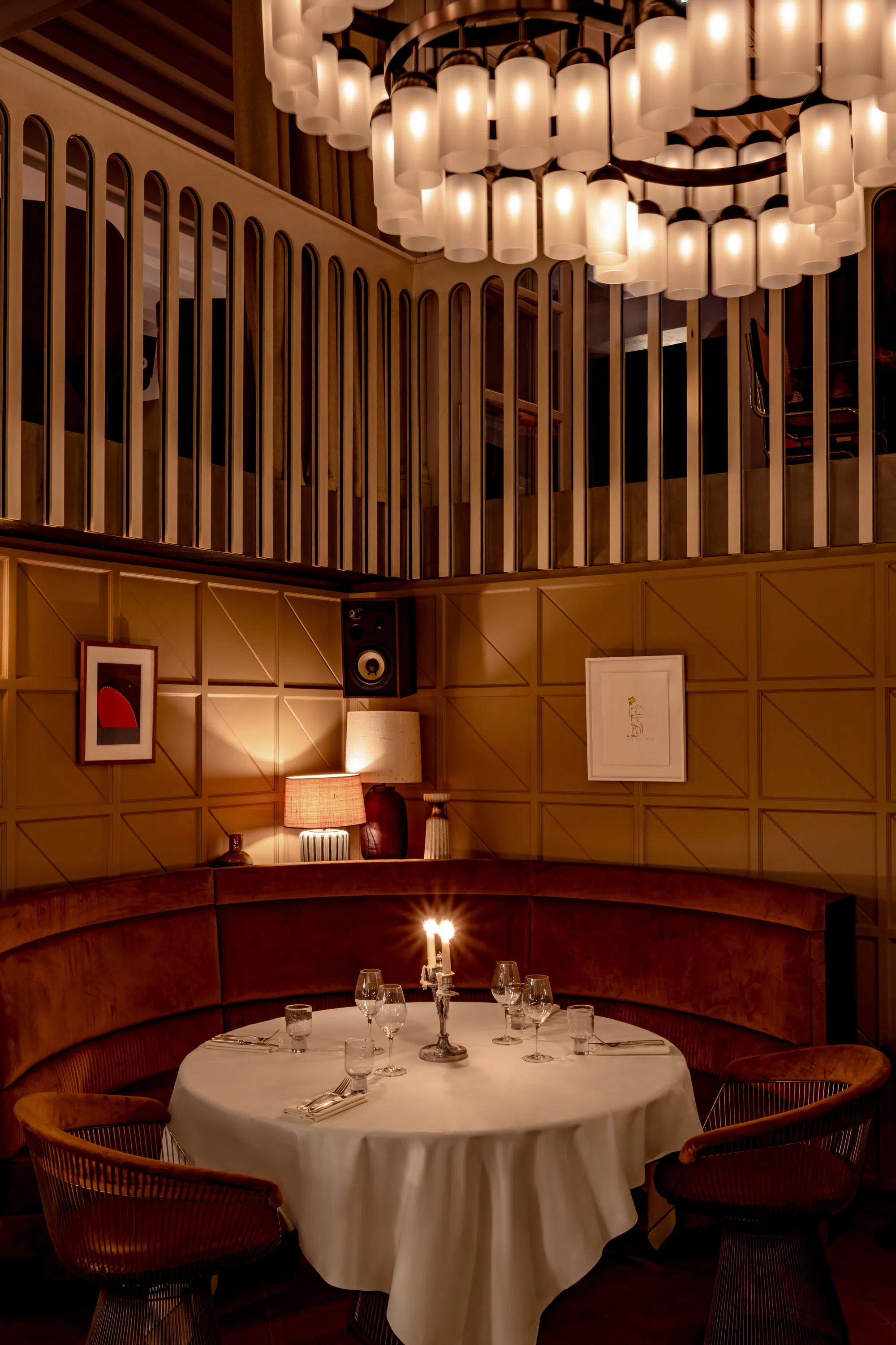 Dimly lit round restaurant table with white tablecloth, candles, wine glasses, and brown chairs.
