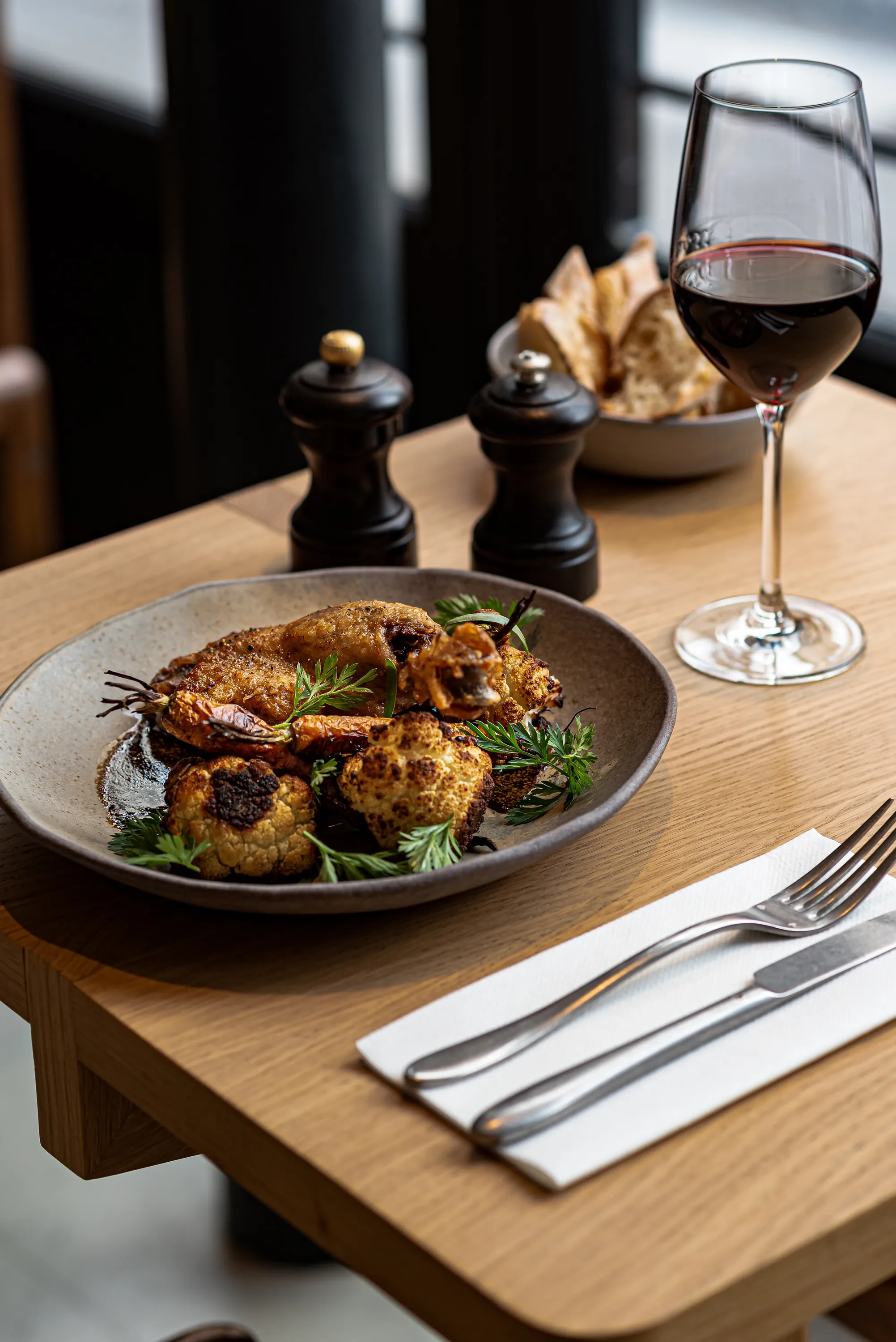 Piatto con pollo arrosto, cavolfiore, erbe aromatiche, carote, bicchiere di vino rosso e pane sul tavolo di legno.
