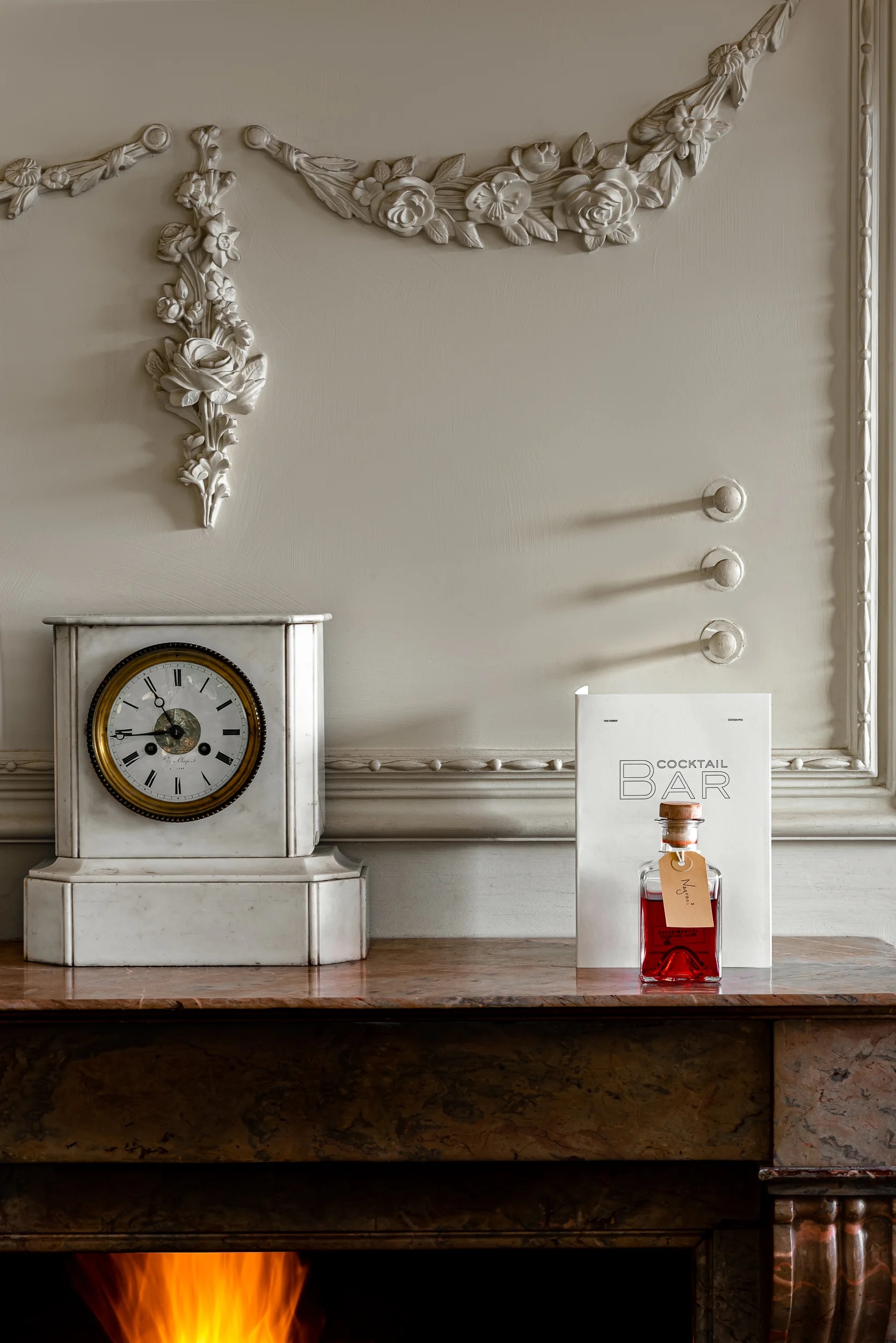 Mensola in marmo con orologio vintage, insegna da cocktail bar, bottiglia rossa per bevande e decorazioni murali floreali scolpite.